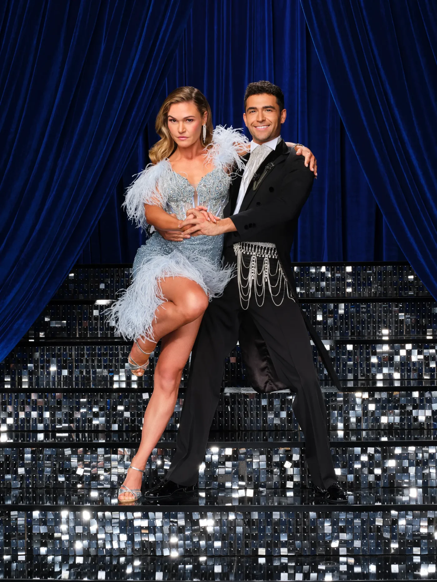 Julia Stiles and Ezra Sosa pose together on a glittering staircase in front of blue curtains.