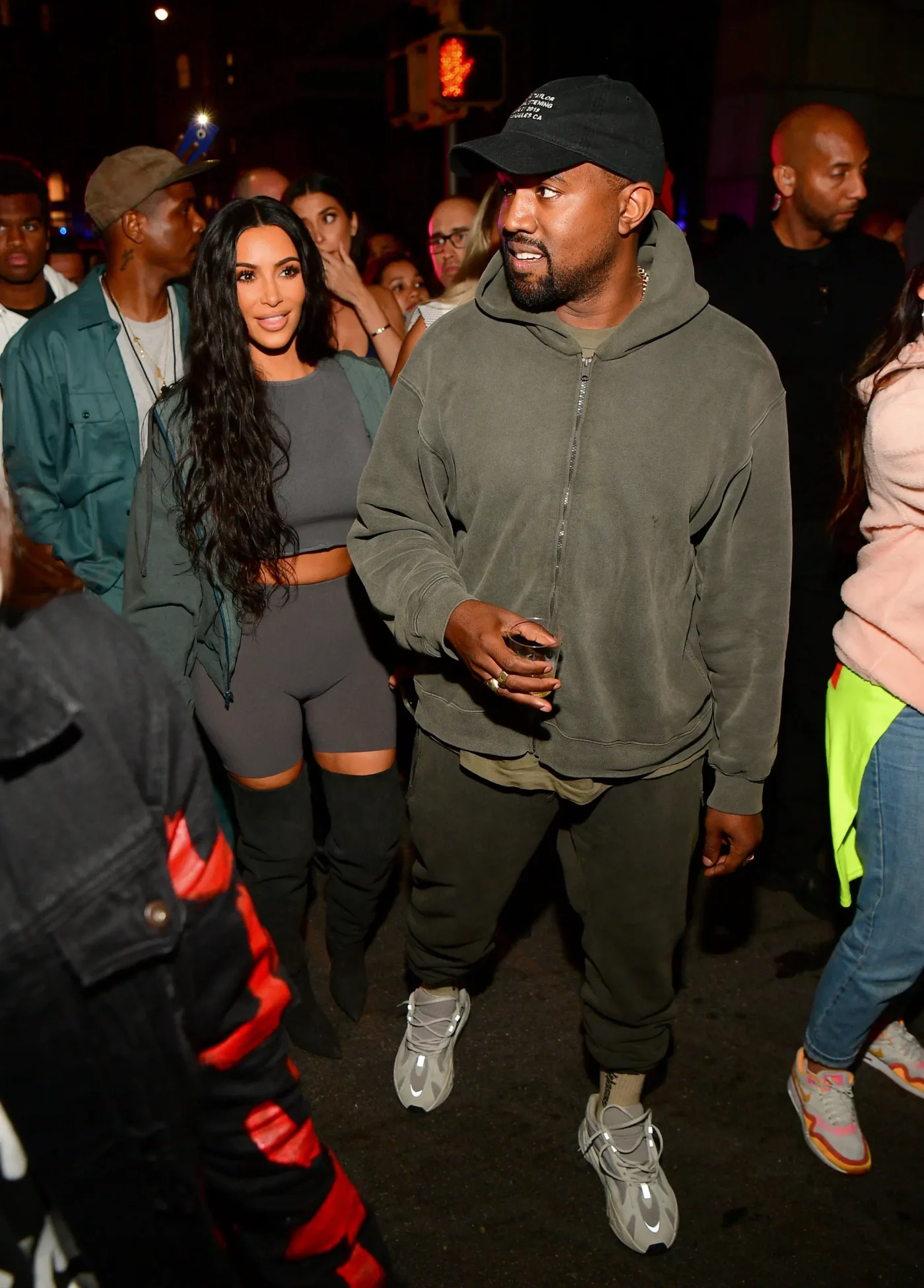 Kanye West and Kim Kardashian walking outside among a crowd.