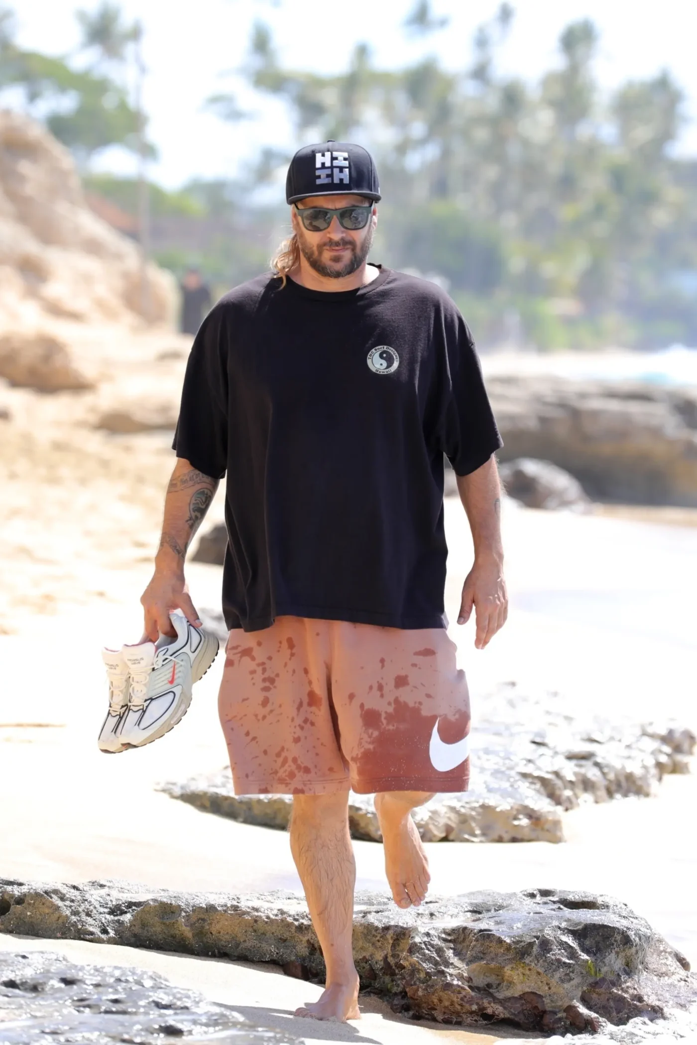 Kevin Federline walks barefoot on a beach in Hawaii, carrying his sneakers.