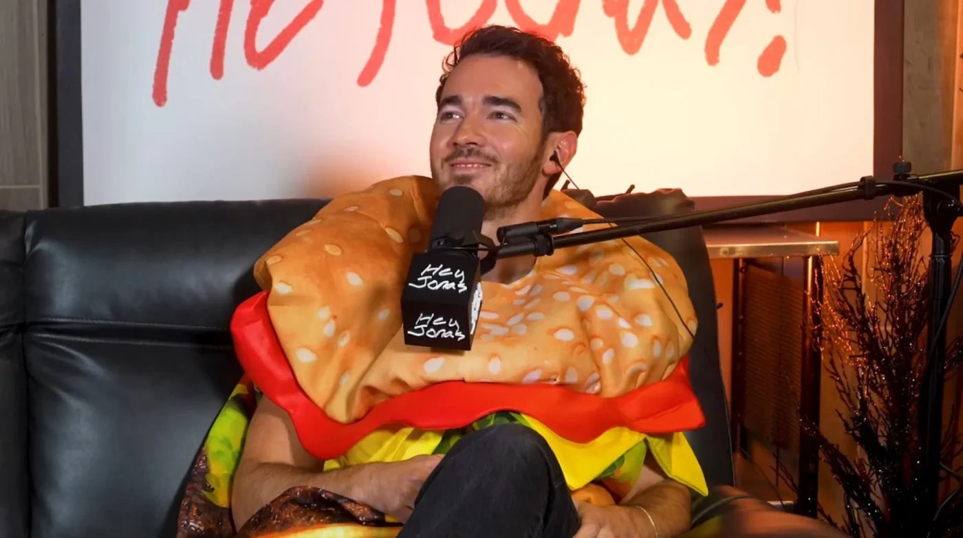 Kevin Jonas wearing a hamburger costume while sitting on a couch.