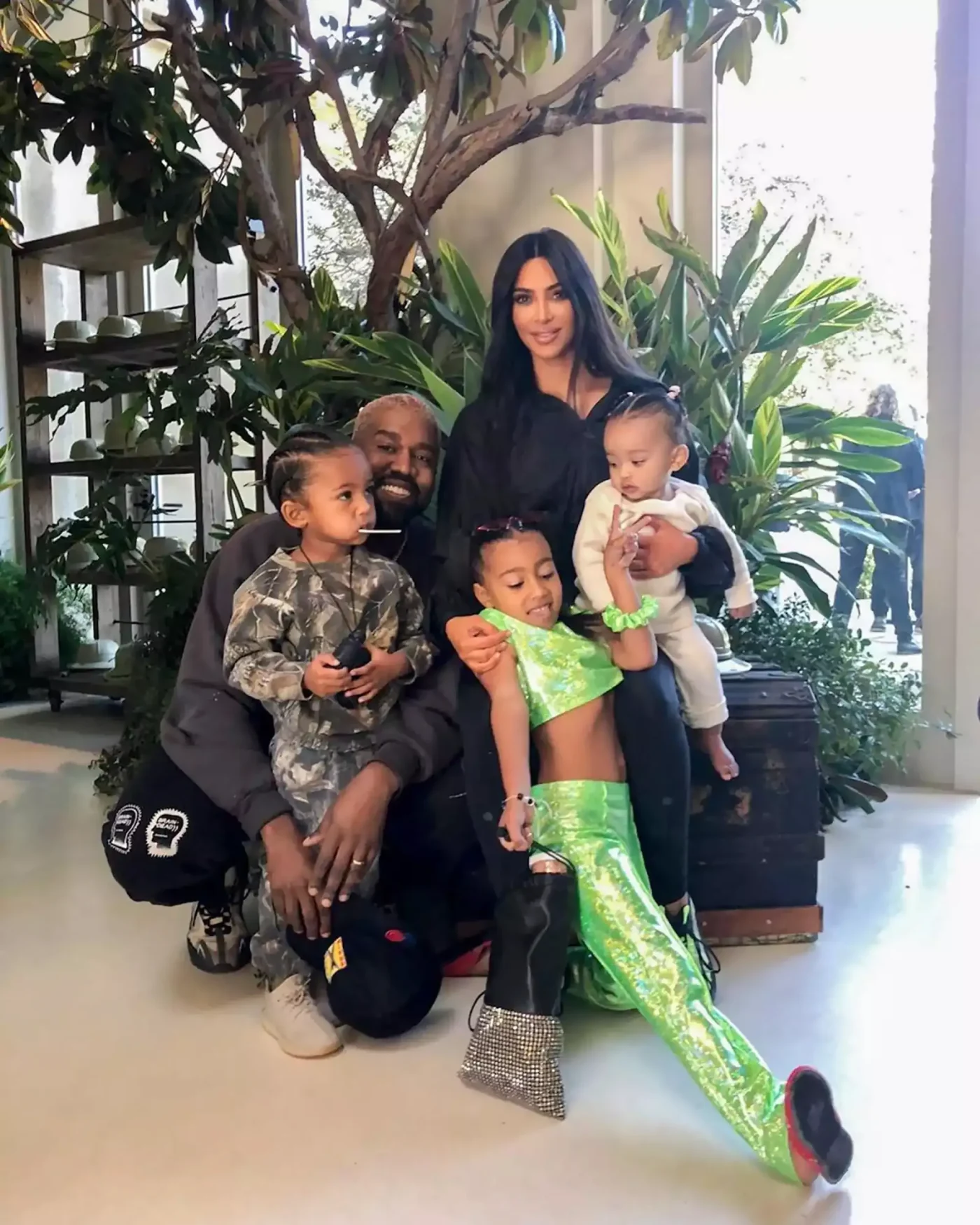 Kim Kardashian and Kanye West pose with their children in a plant-filled room.