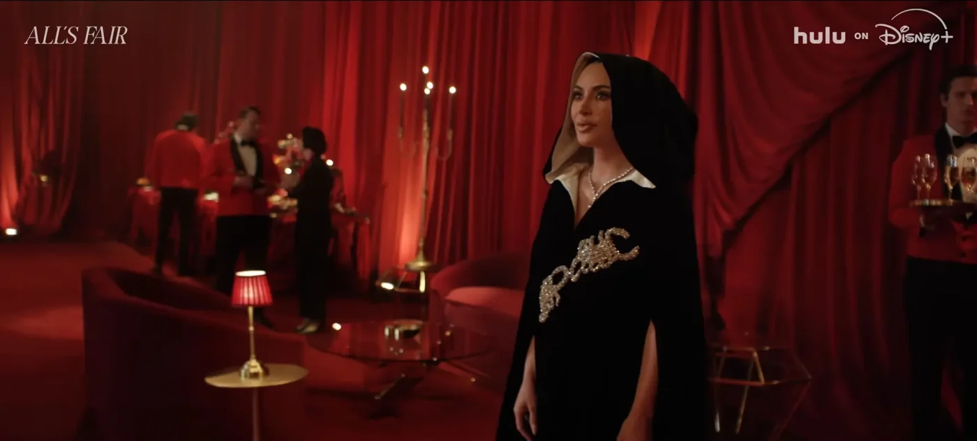 Kim Kardashian wearing a black hooded cape in a red-draped room for