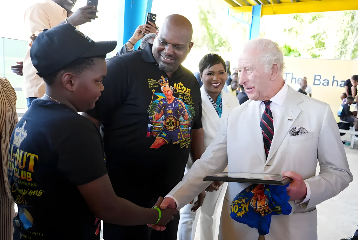 King Charles laughs as he is presented with a novelty T-shirt depicting himself in boxing shorts, gloves, and a crown during a visit to The Bahamas Boxing Academy in Nassau. Meeting with 12-year-old Sanai Miller and coach Jermaine Gibson, the monarch's easy humour and warmth were on full display