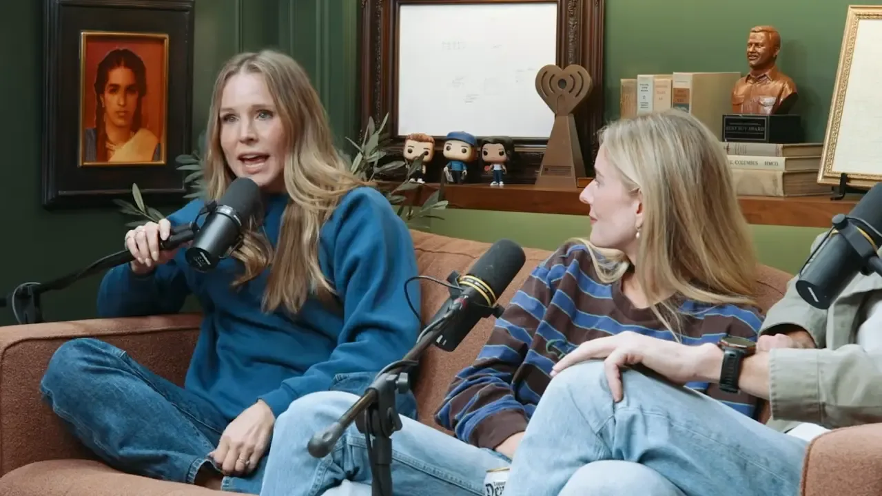 Kristen Bell speaking into a microphone while sitting on a couch with other guests.