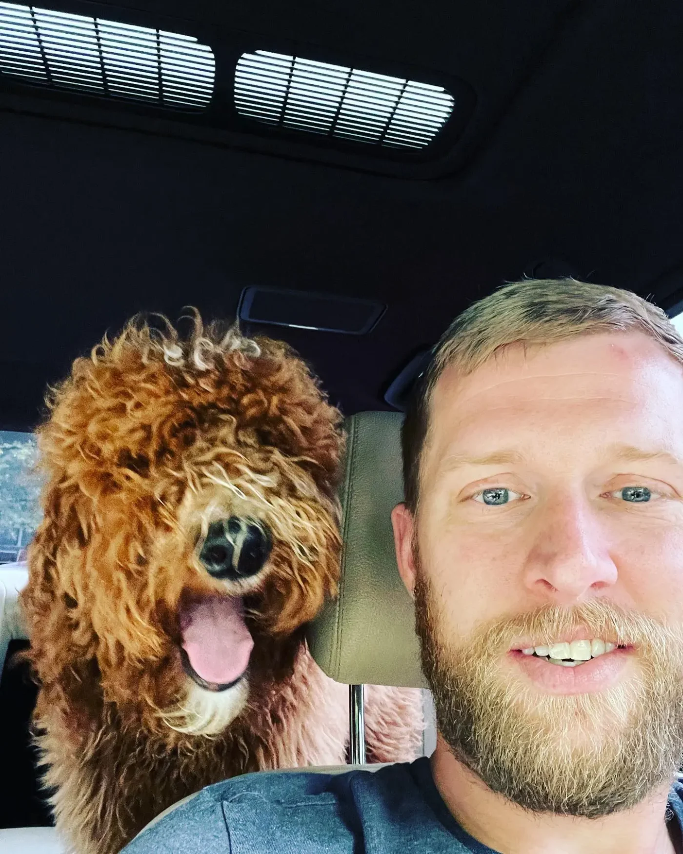Kyle Chrisley taking a selfie in a car with a fluffy brown dog with its mouth open.