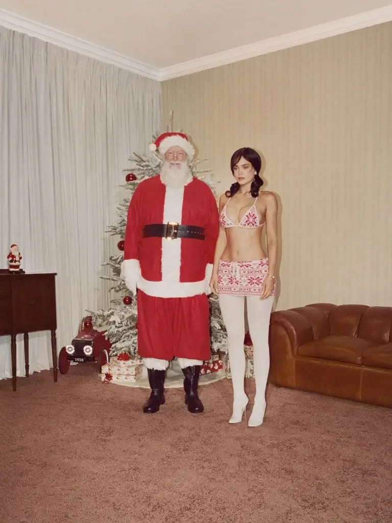 Kylie posing in festive lingerie in living room next to Santa