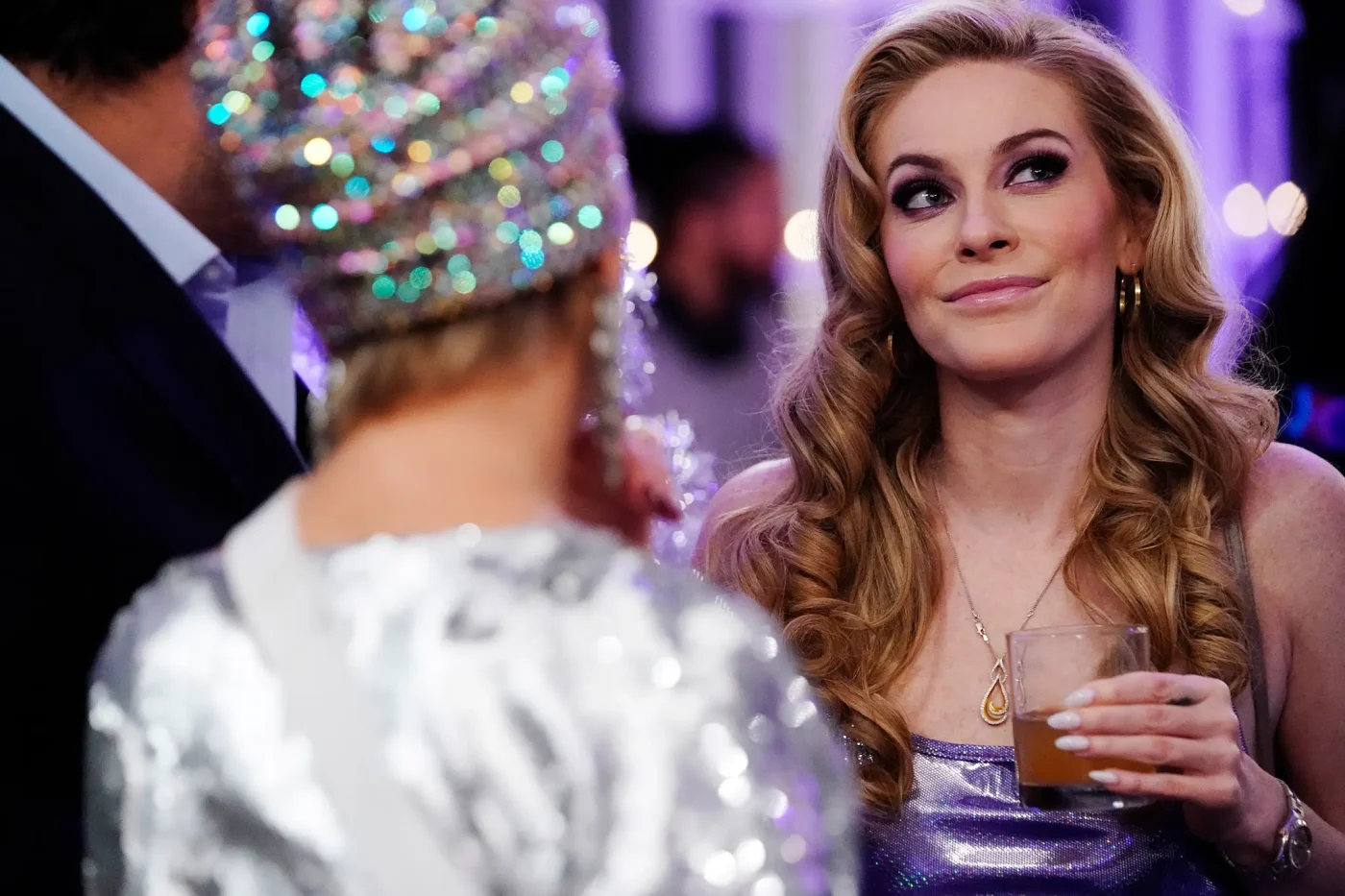 Leah McSweeney holding a drink while looking at someone wearing a sequined outfit.