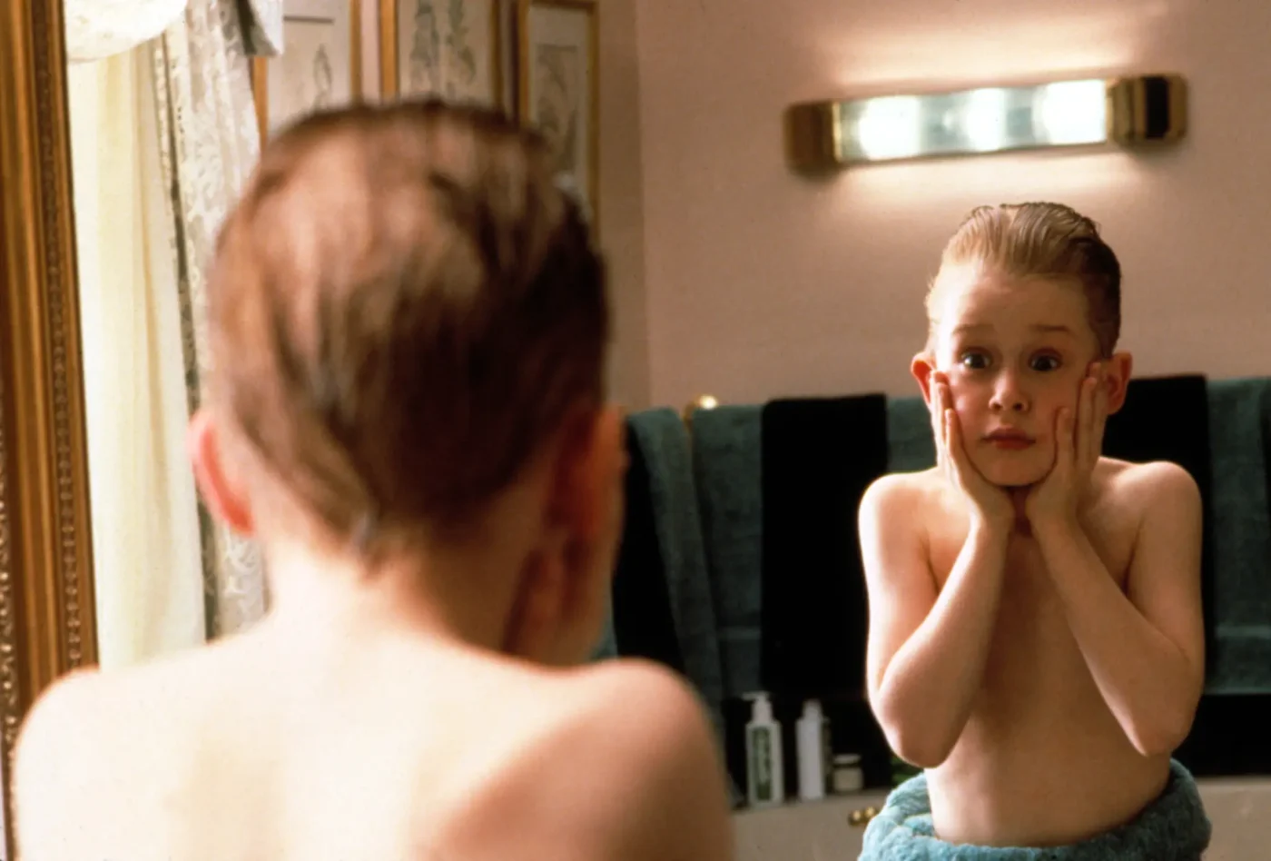 Macaulay Culkin as Kevin McCallister in Home Alone, reacting with shock in the bathroom mirror after applying aftershave lotion.