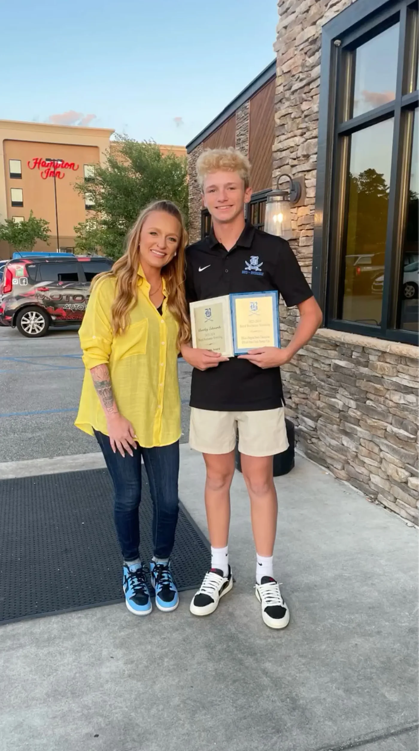 Maci Bookout standing next to her son Bentley, who is holding two achievement plaques.