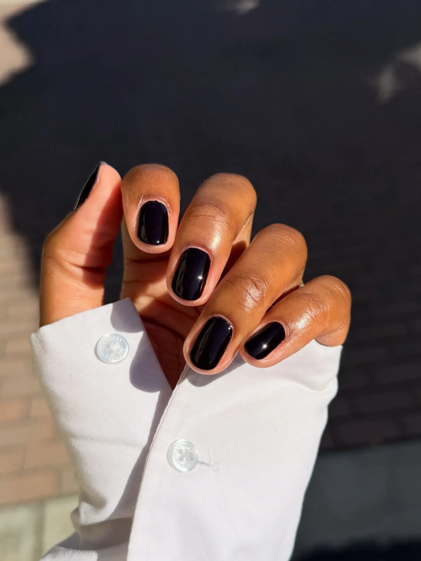 Manicured hand with dark polished nails wearing a white sleeve