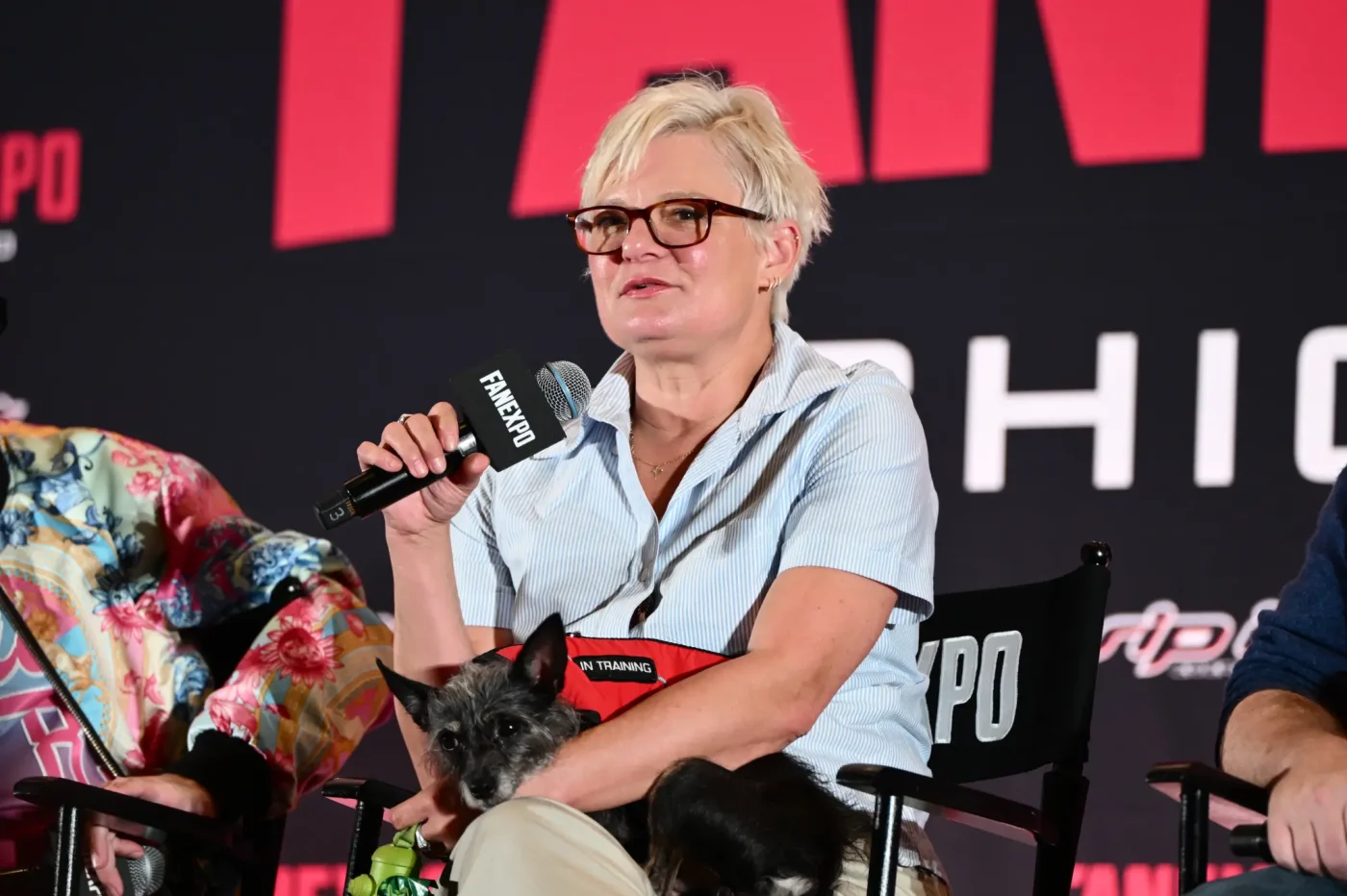 Martha Plimpton speaks into a microphone while holding a small dog wearing an