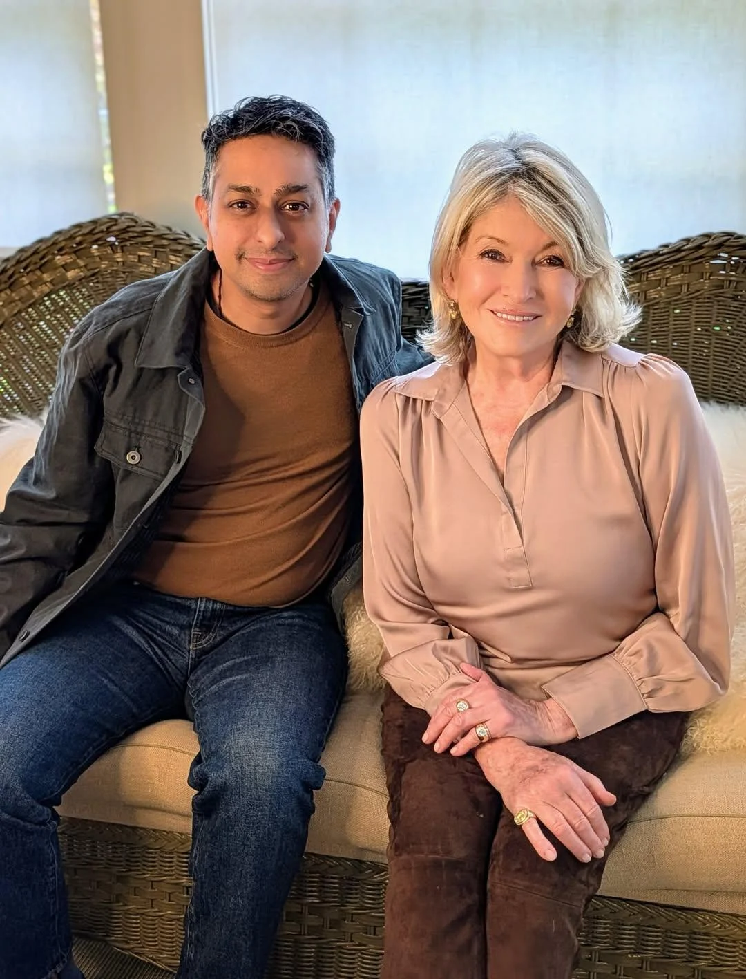 Martha Stewart and a man sitting side by side on a wicker couch, with Martha Stewart wearing a pink silk shirt.