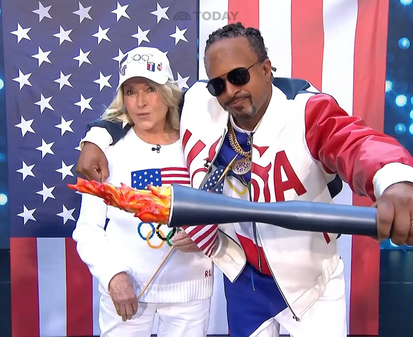 Martha Stewart and Snoop Dogg holding an Olympic torch in front of an American flag.