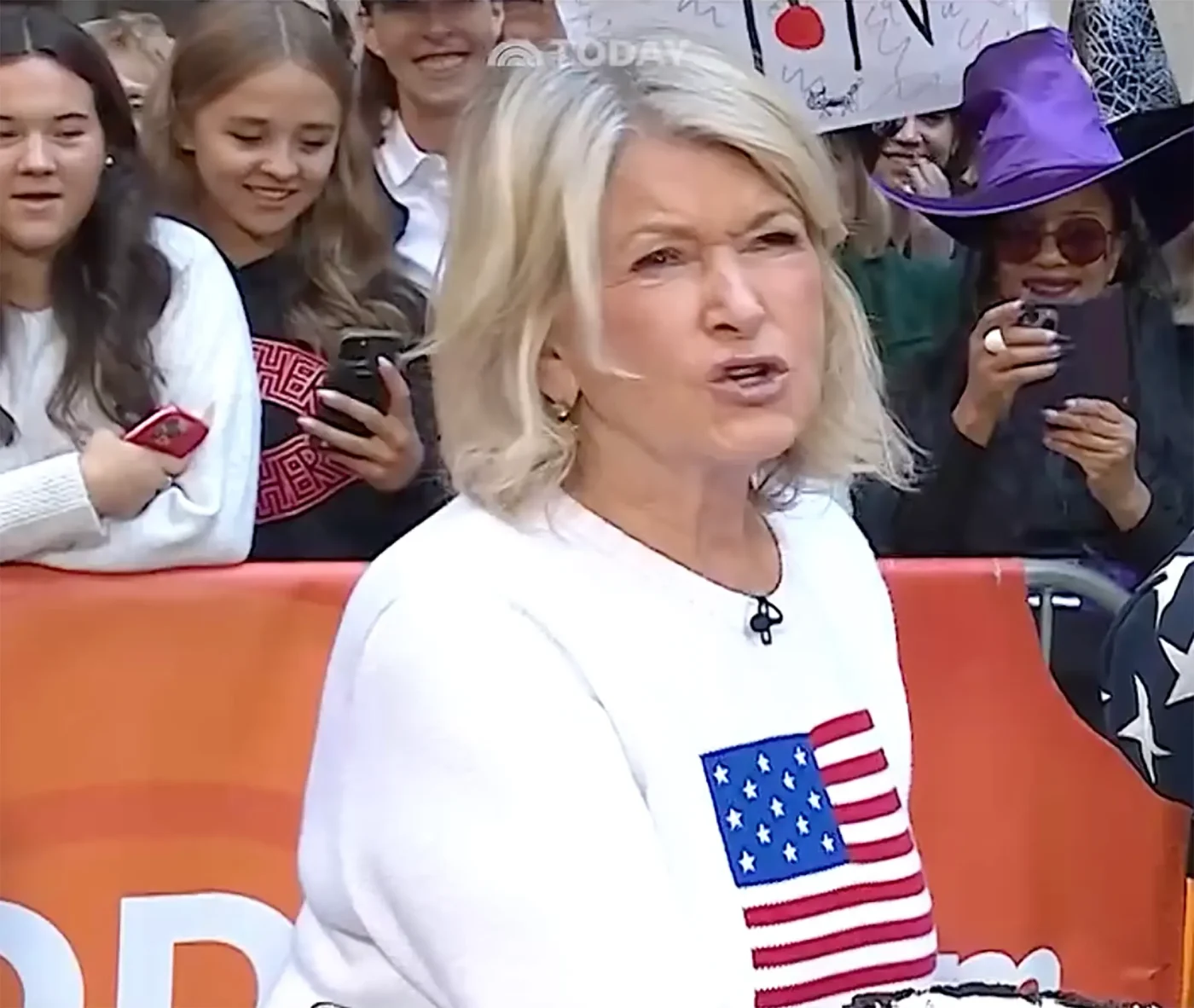Martha Stewart wearing a white sweater with an American flag patch speaking on the