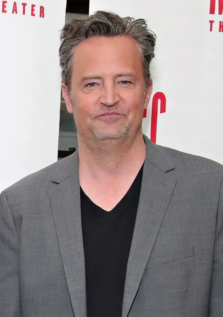 Matthew Perry smiling, wearing a black shirt and gray blazer.