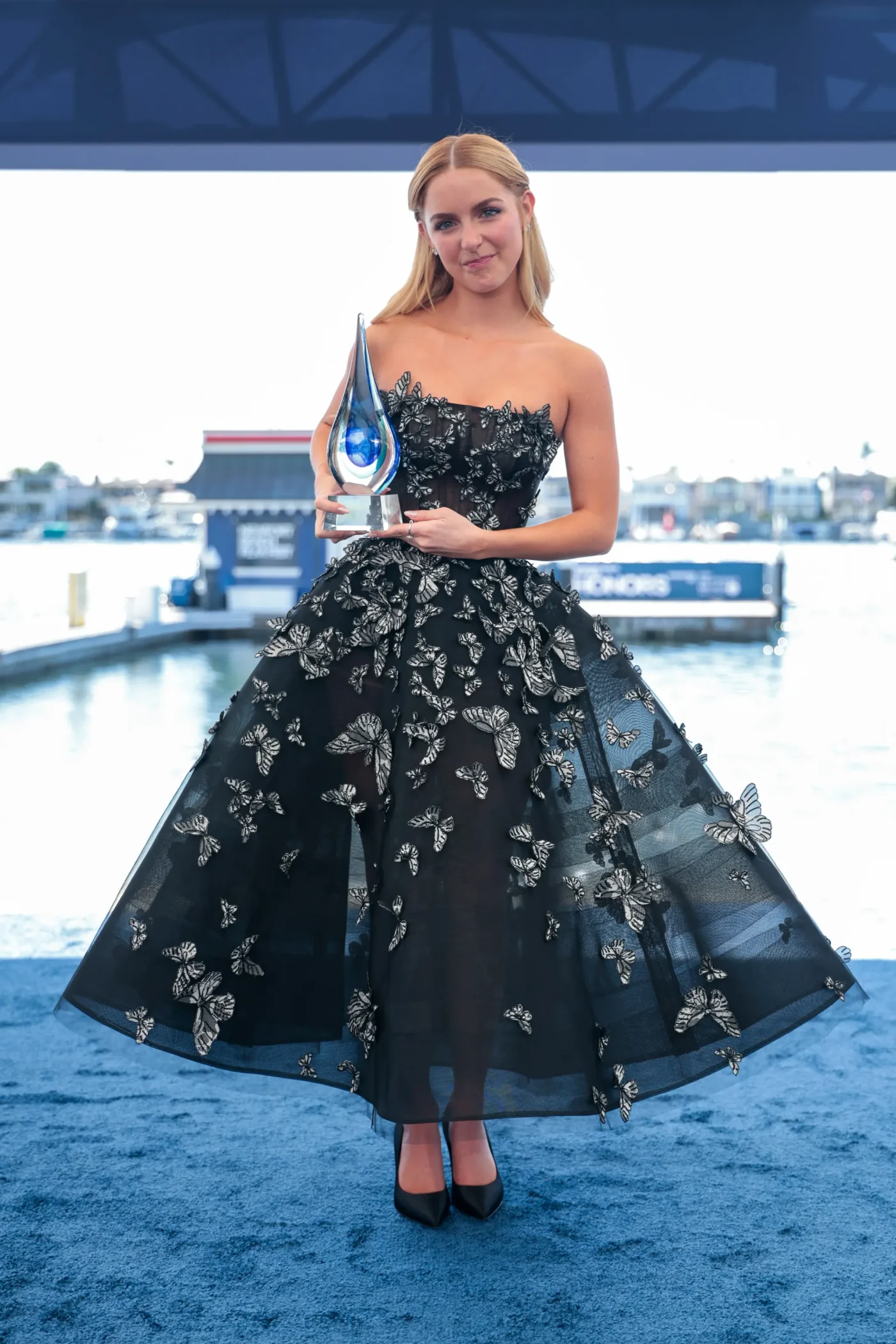 McKenna Grace holds an award, wearing a black strapless gown covered in white butterfly appliques.