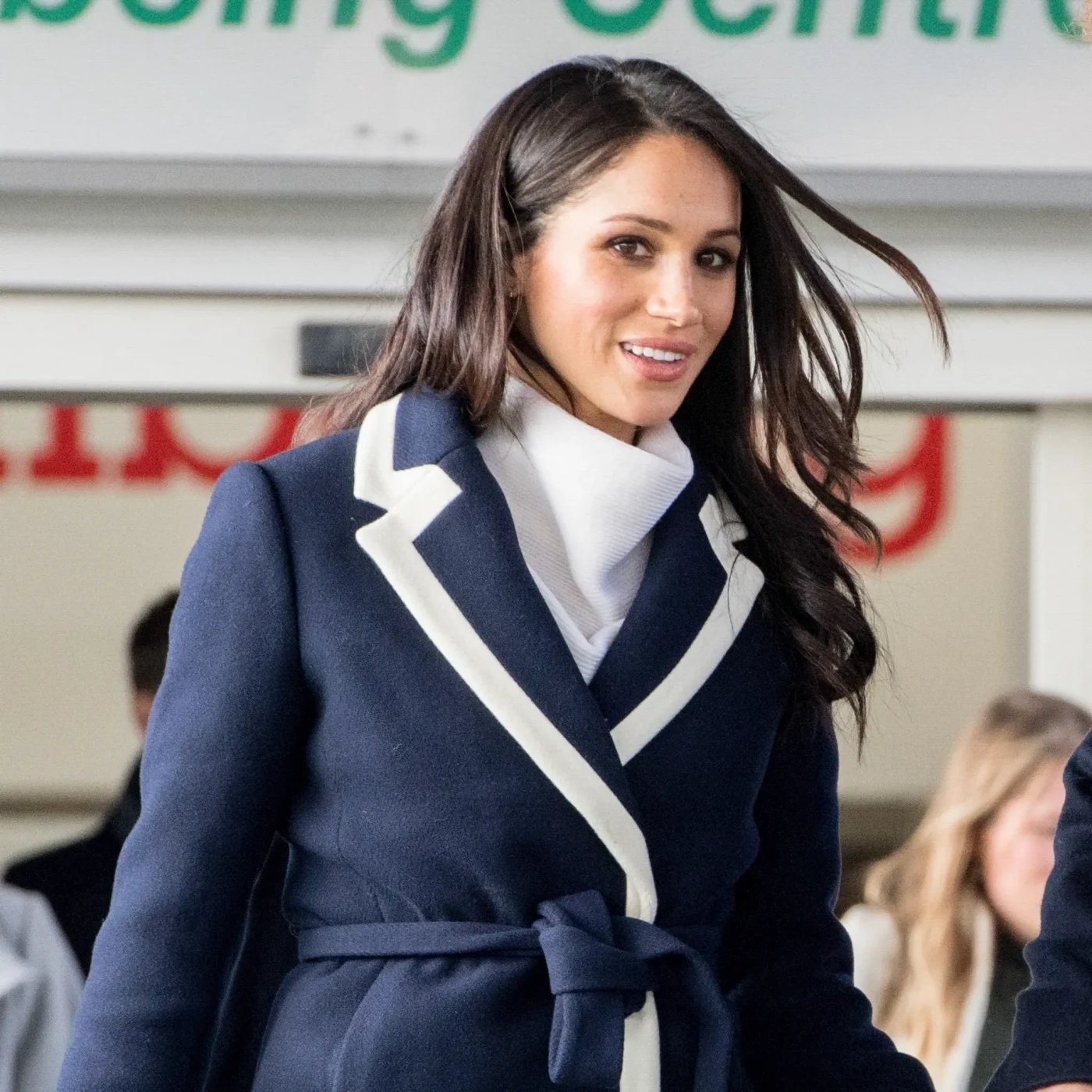Meghan Markle wearing a dark blue coat with white trim and a white turtleneck.