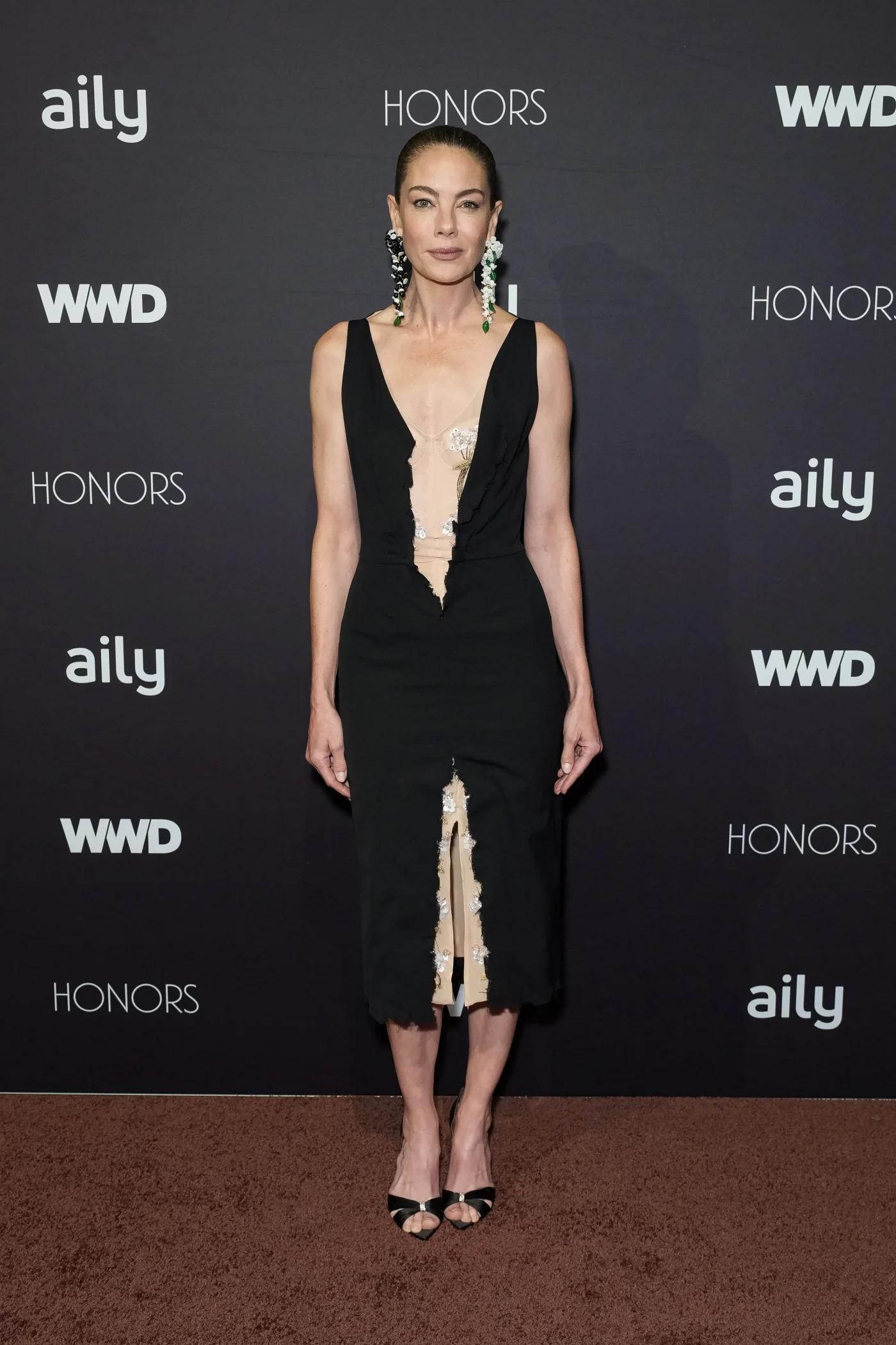 Michelle Monaghan poses in a black dress with sheer inserts at the WWD Honors.