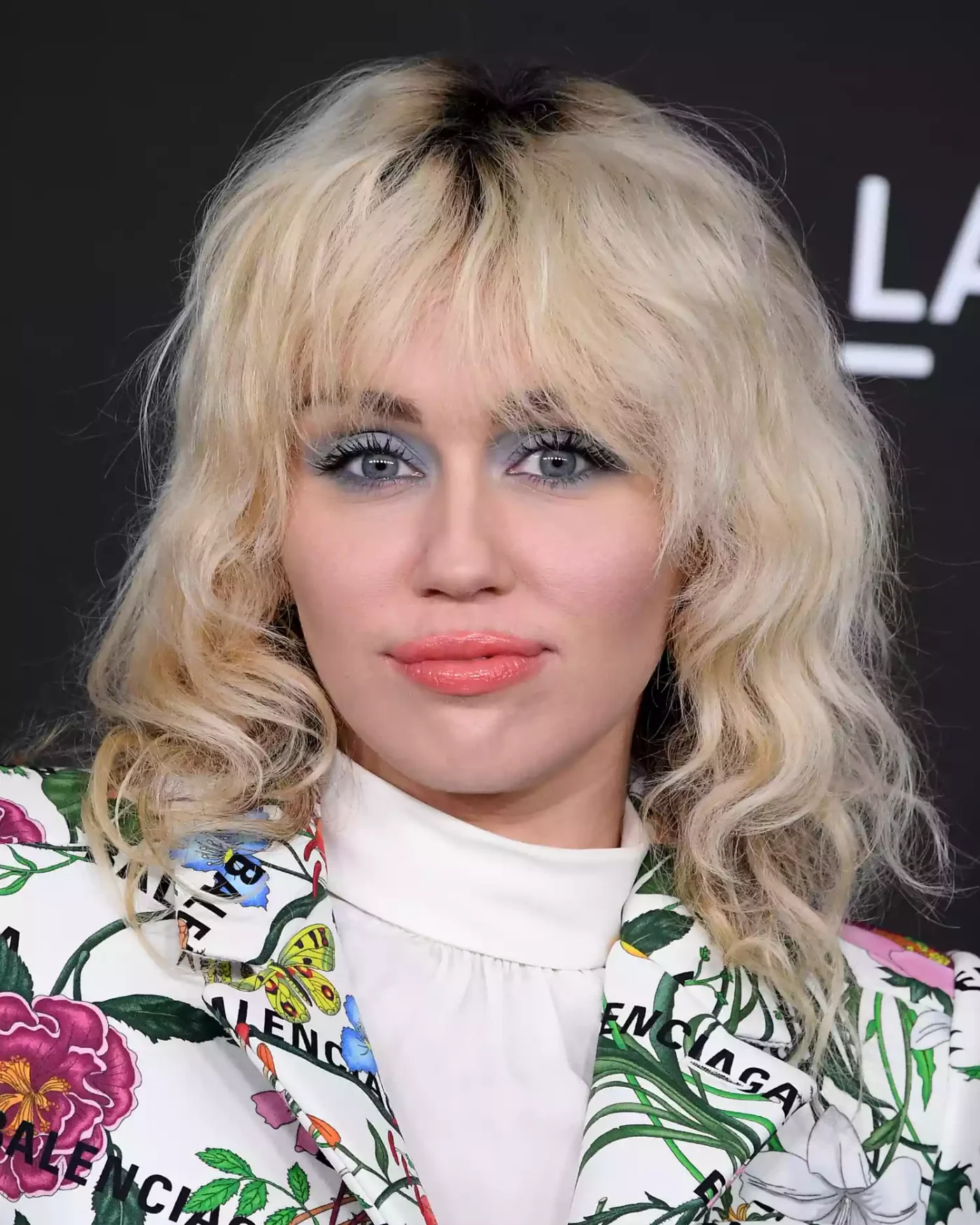 Miley Cyrus wears a wavy blonde shag with grown-out roots, a