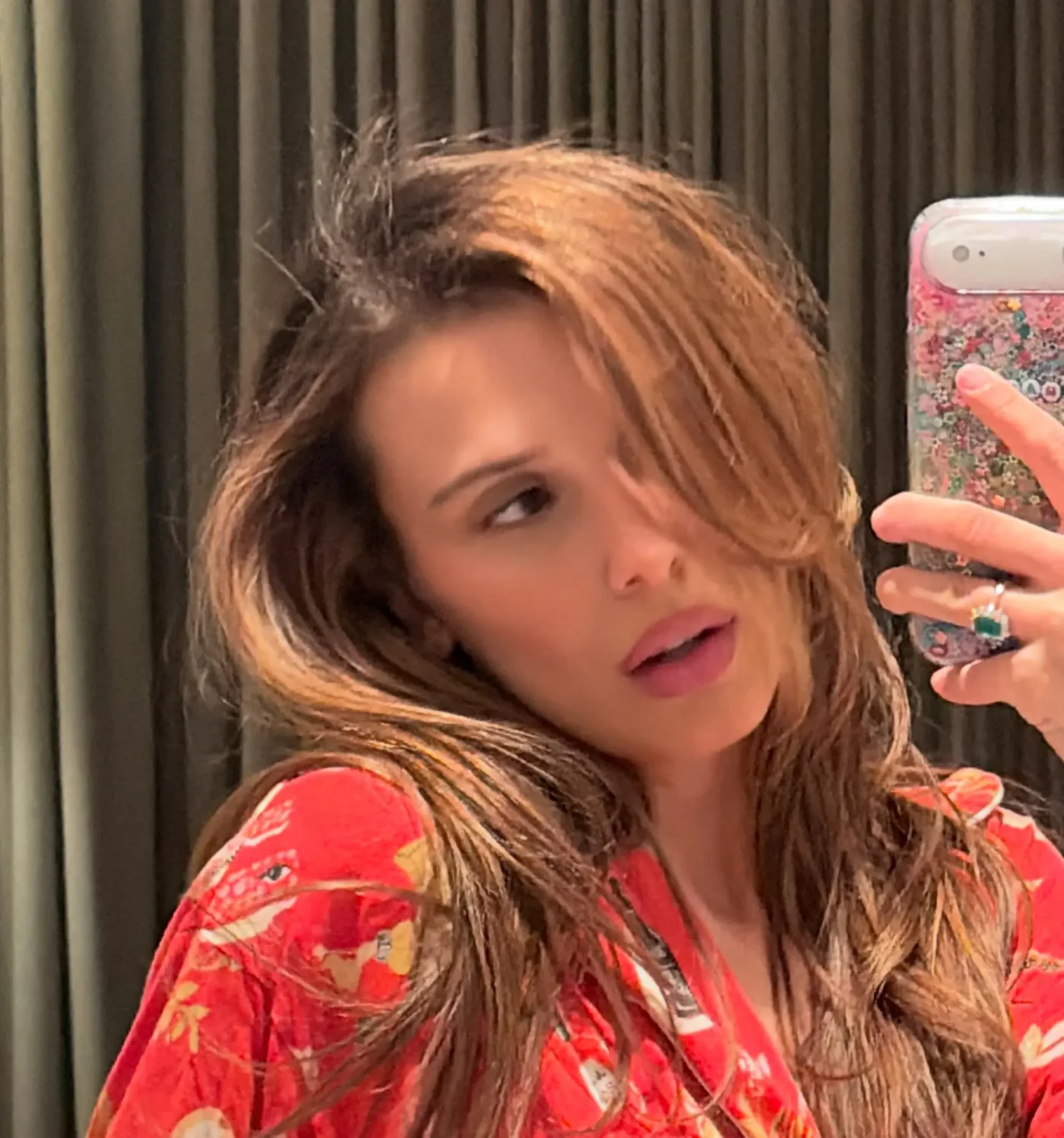Millie Bobby Brown takes a selfie in a mirror, wearing a red patterned top.