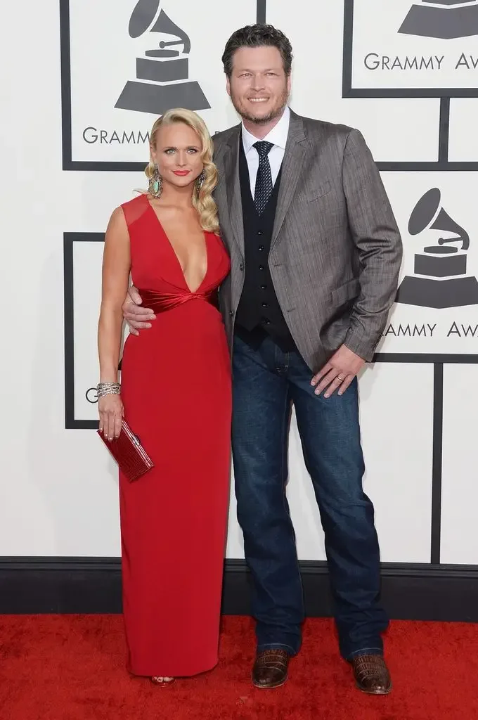 Miranda Lambert wearing a red dress on the Grammys red carpet next to Blake Shelton in a grey jacket and jeans