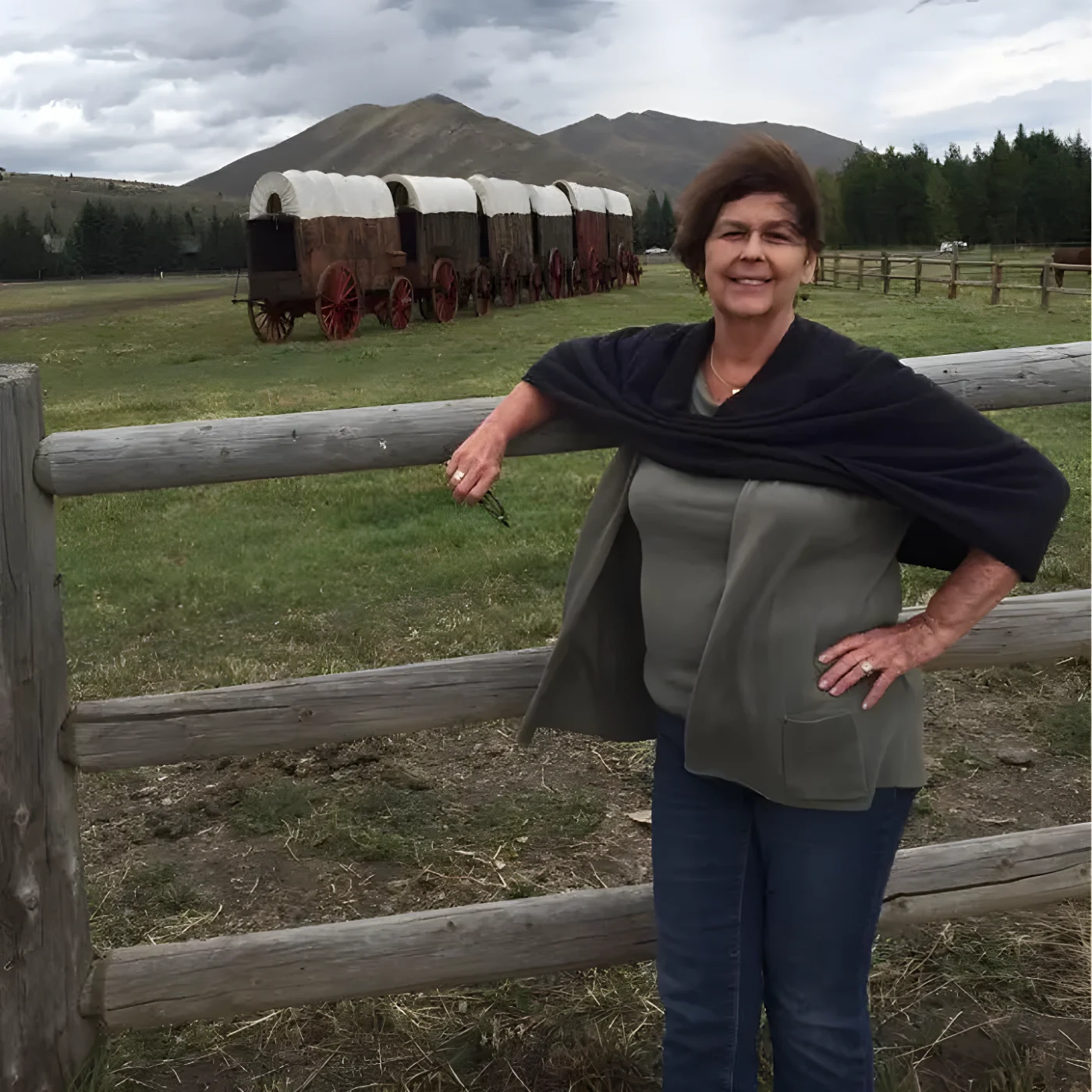Nancy Guthrie standing by a wooden fence with covered wagons and mountains in the background.