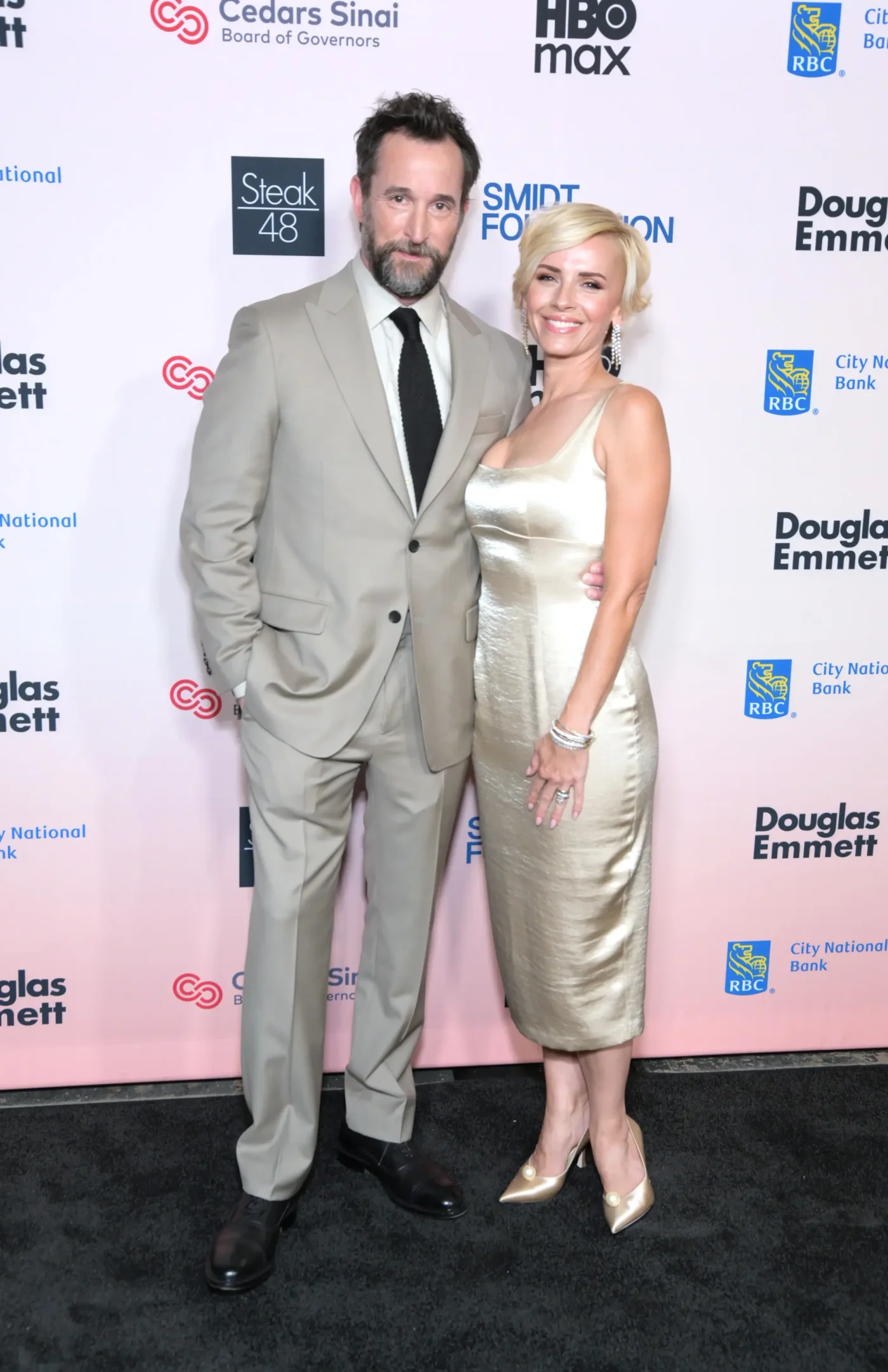 Noah Wyle and Sara Wells pose on the red carpet at the Cedars-Sinai Board of Governors Sunset Soirée.