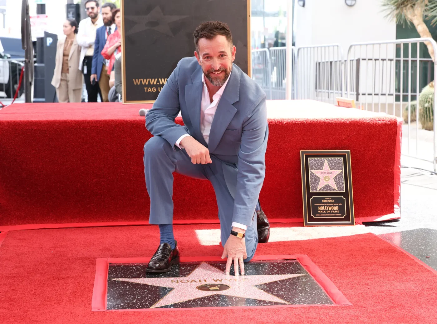 Noah Wyle kneels next to his star on the Hollywood Walk of Fame.