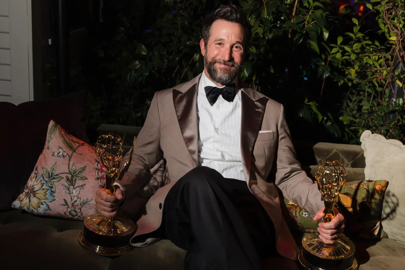 Noah Wyle seated with Emmy statuettes in each hand.