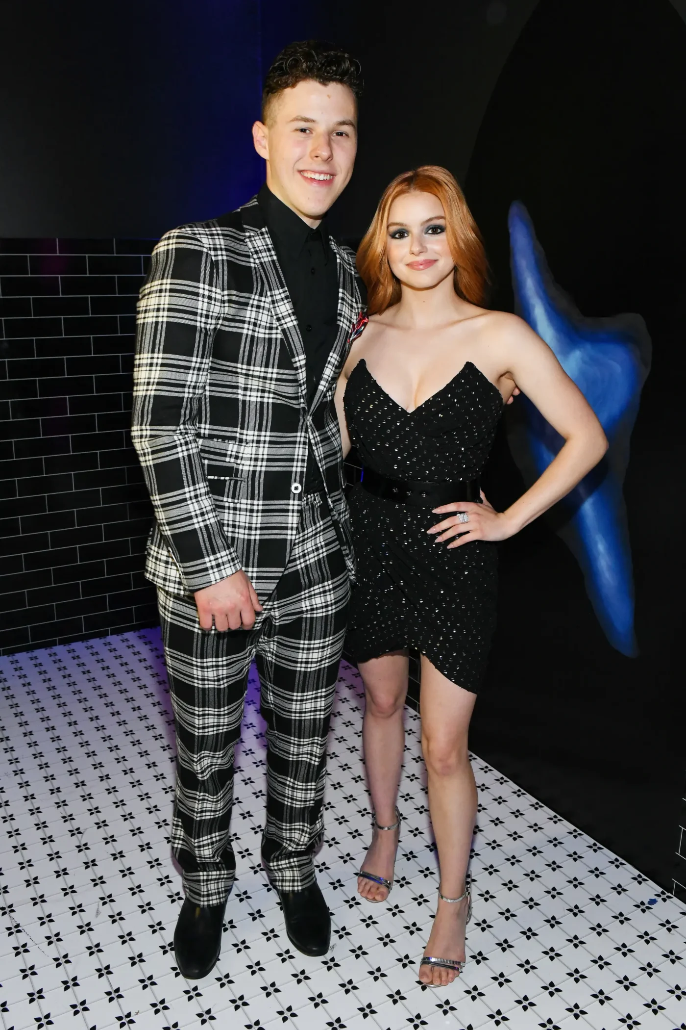Nolan Gould and Ariel Winter standing together, with Gould in a black and white plaid suit and Winter in a black strapless dress.