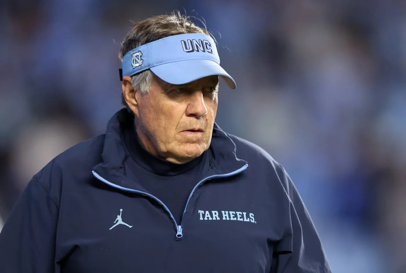 North Carolina Tar Heels head coach Bill Belichick wearing a light blue UNC visor and a dark blue jacket.
