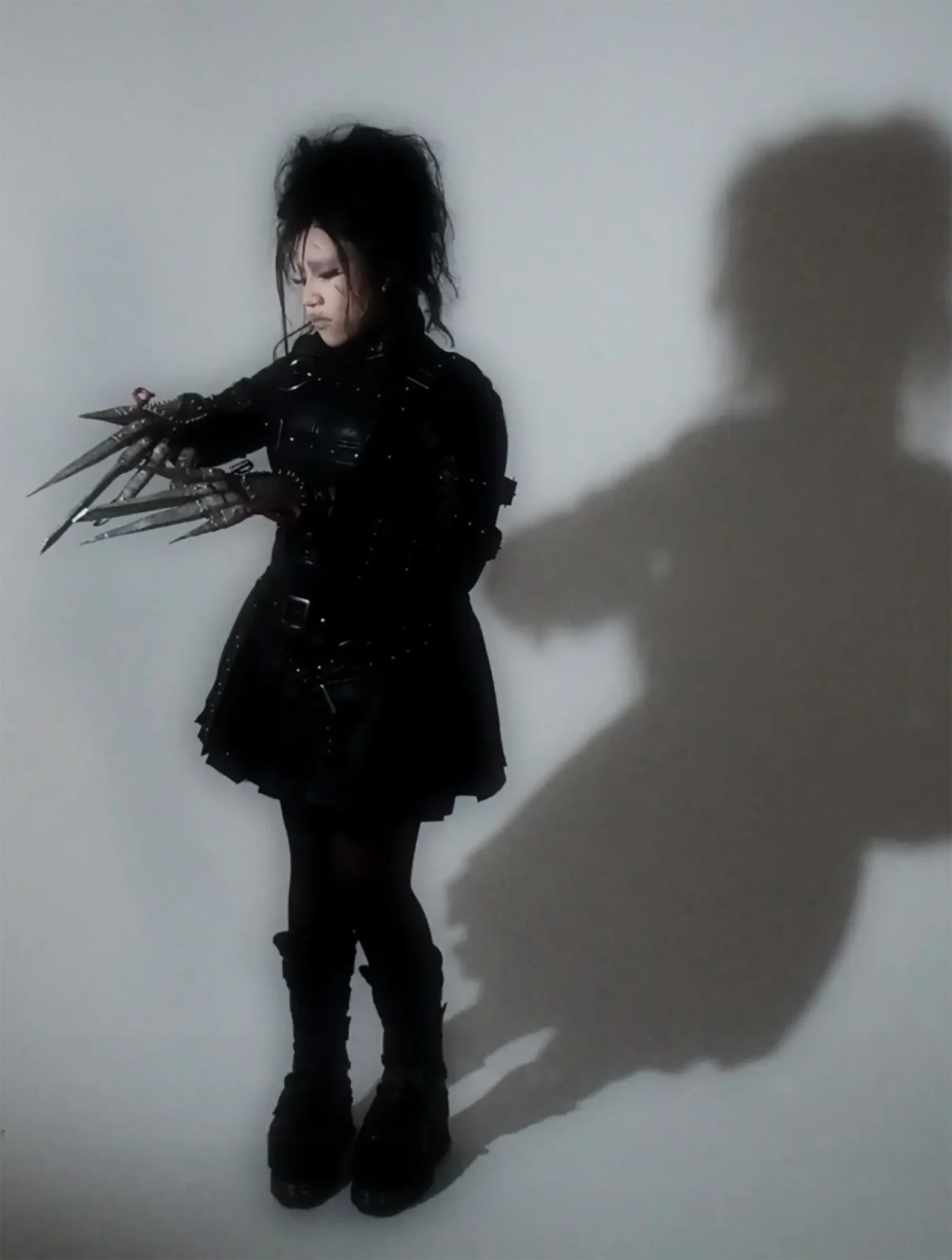North West dressed in an Edward Scissorhands costume, featuring spiked hair, a black leather outfit, and scissor-like hand attachments.