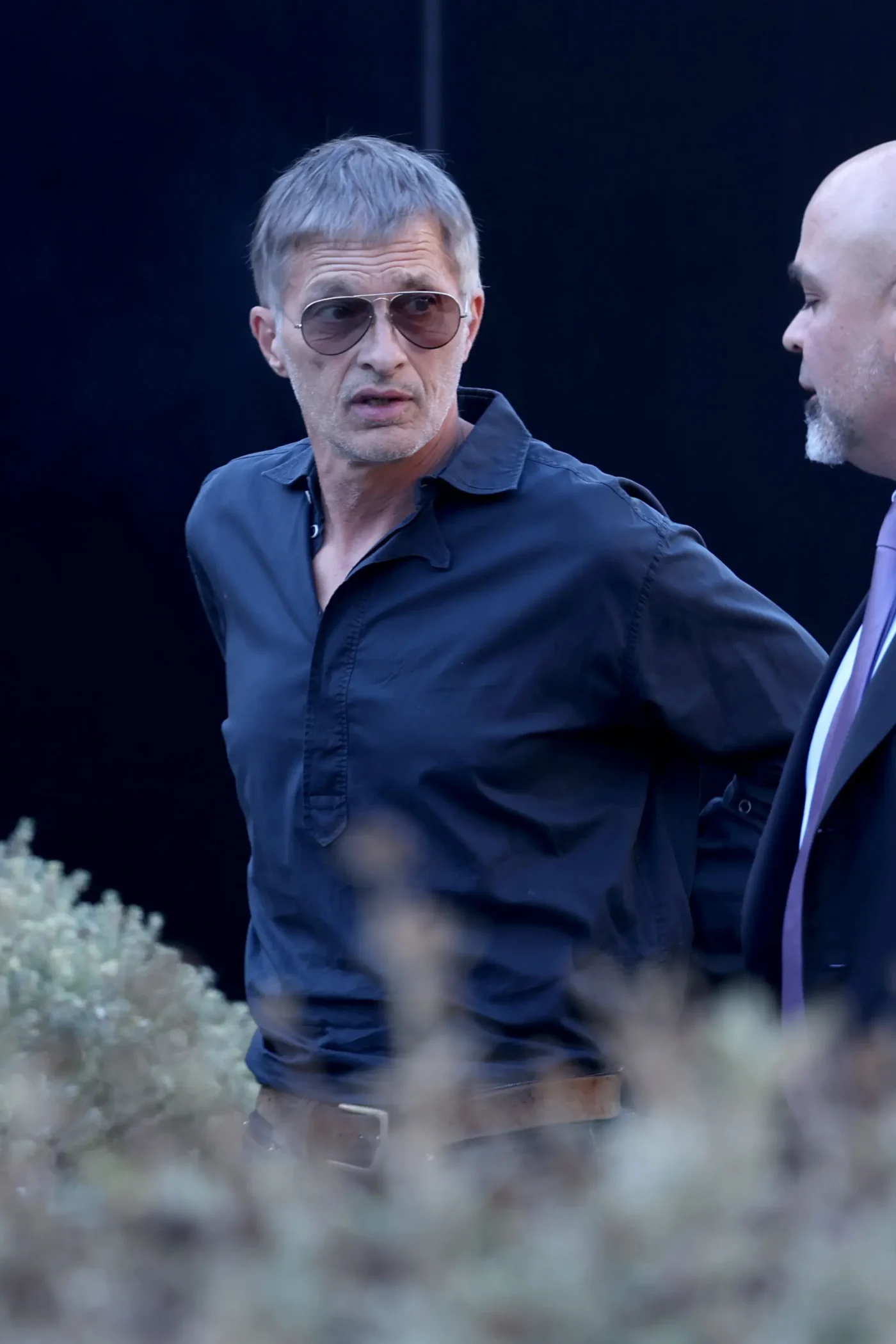 Olivier Martinez wearing sunglasses and a dark shirt, talking with his lawyer.