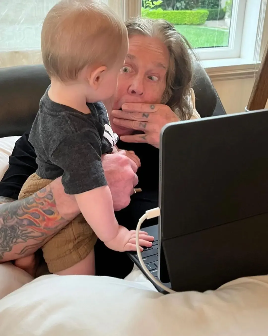 Ozzy Osbourne holds his grandson Sidney as they look at a tablet together.