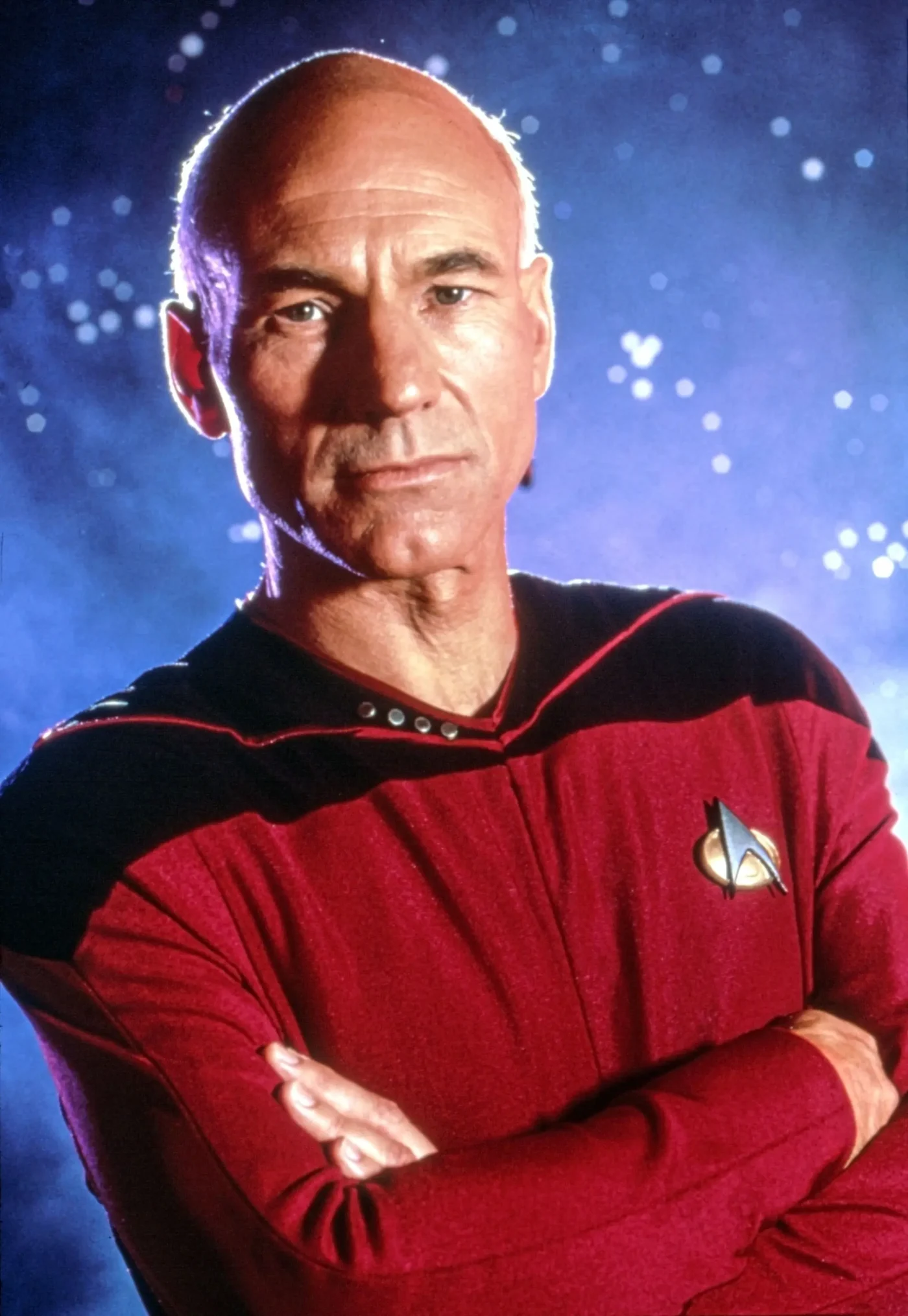 Patrick Stewart as Captain Jean-Luc Picard in Star Trek Nemesis, wearing a red Starfleet uniform against a starry background.