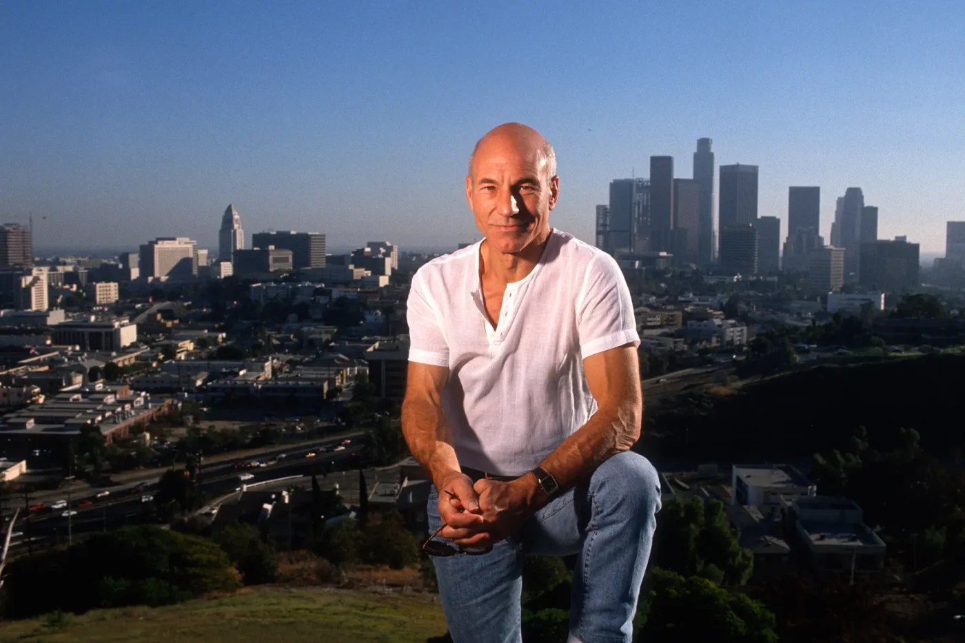 Patrick Stewart kneeling outdoors with the Los Angeles skyline in the background.