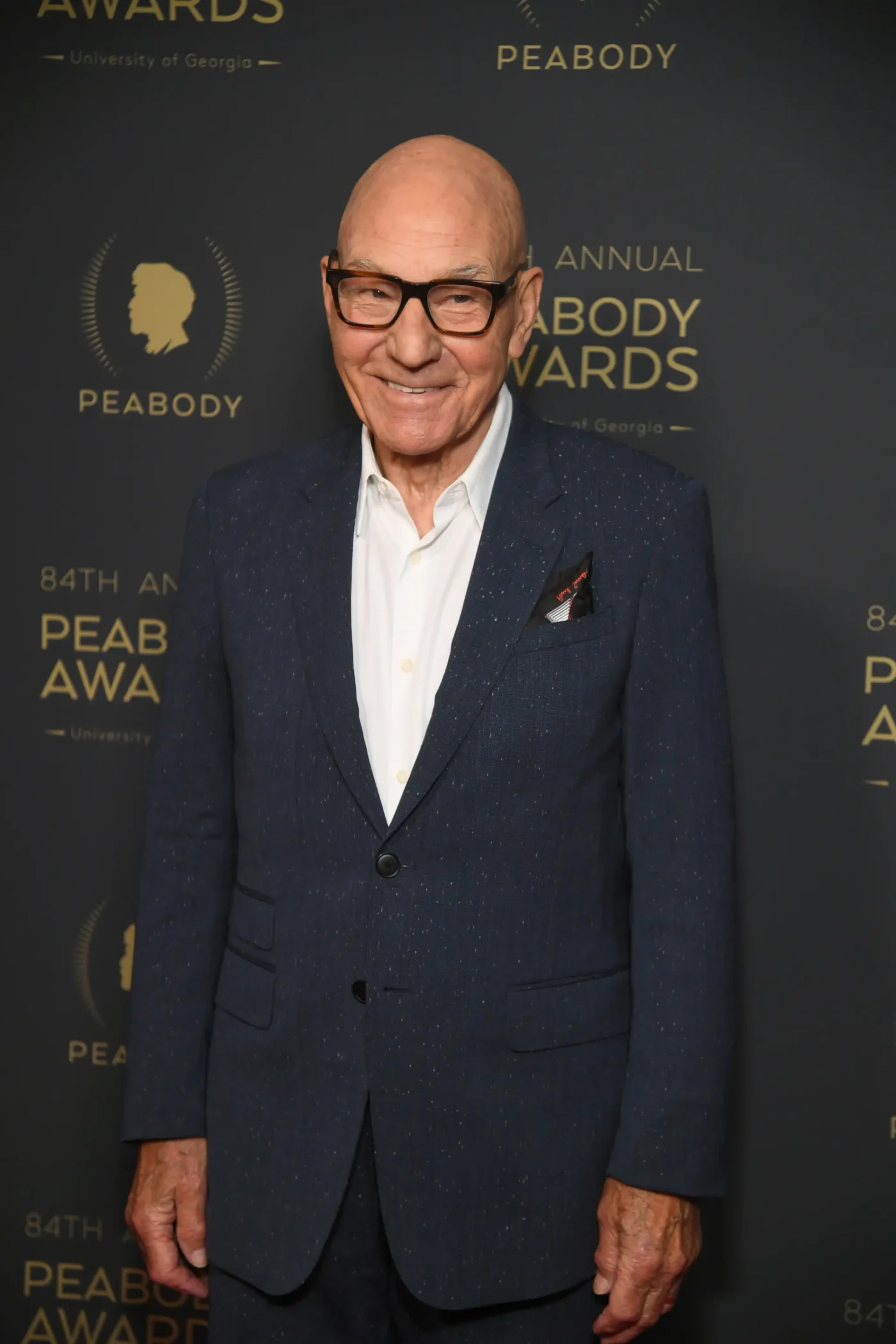 Patrick Stewart smiling in a dark blue suit and white shirt at the Peabody Awards.