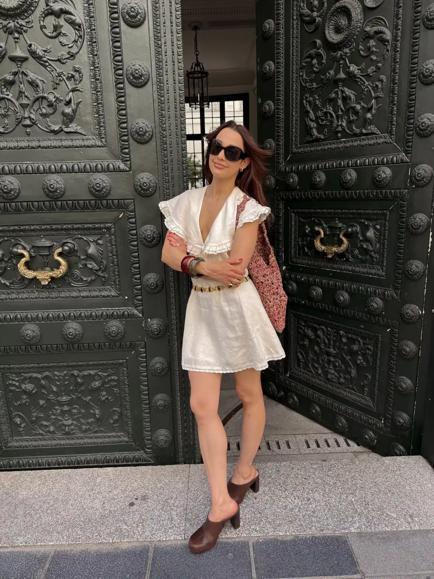 Person standing in front of a decorated doorway wearing sunglasses and a white outfit