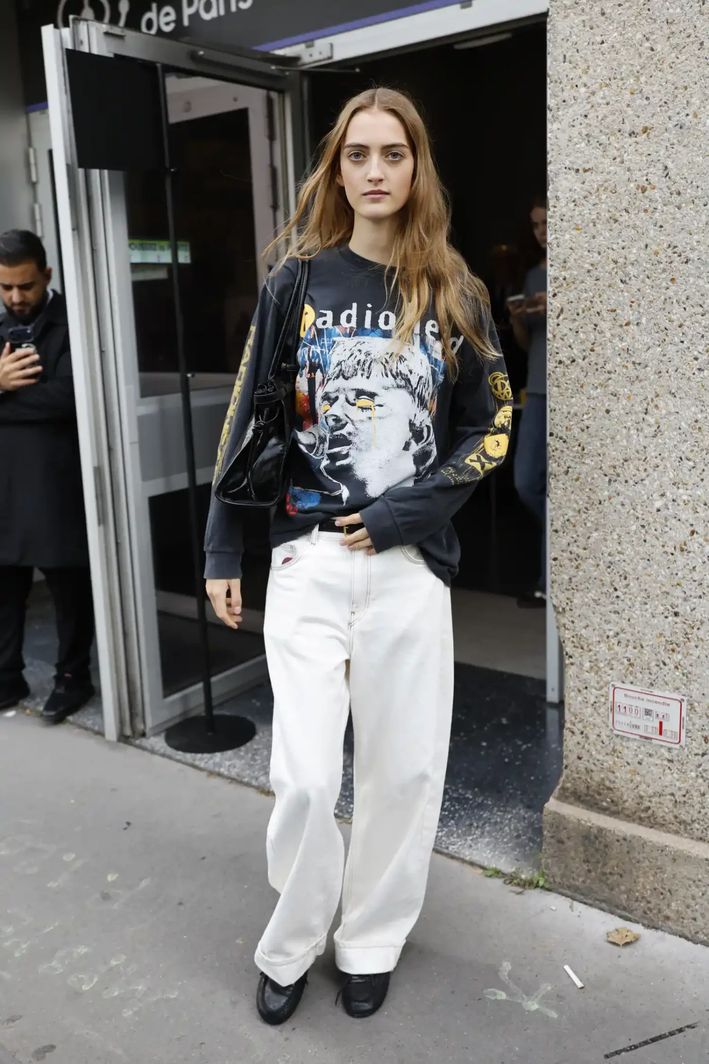 Person standing outdoors wearing a graphic sweatshirt and white trousers