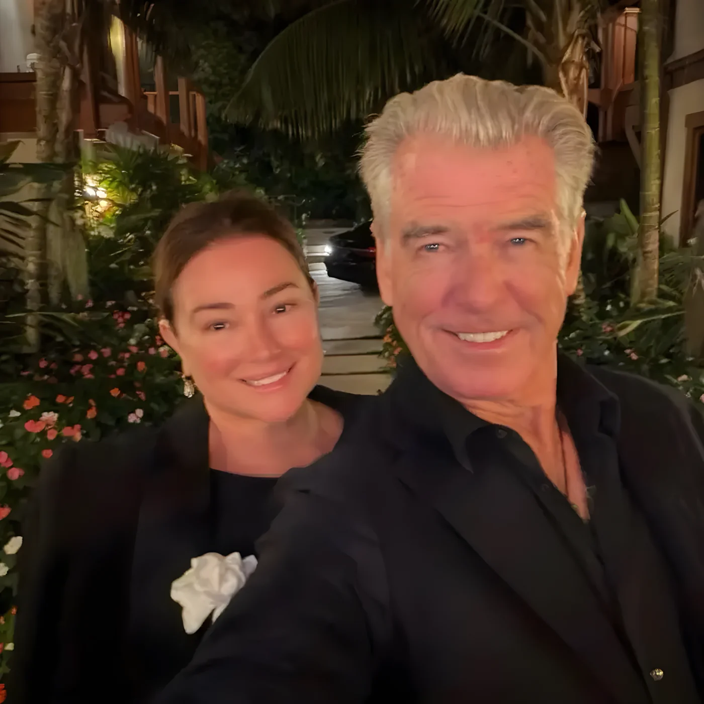 Pierce Brosnan and Keely Shaye Smith smiling in a tropical setting.