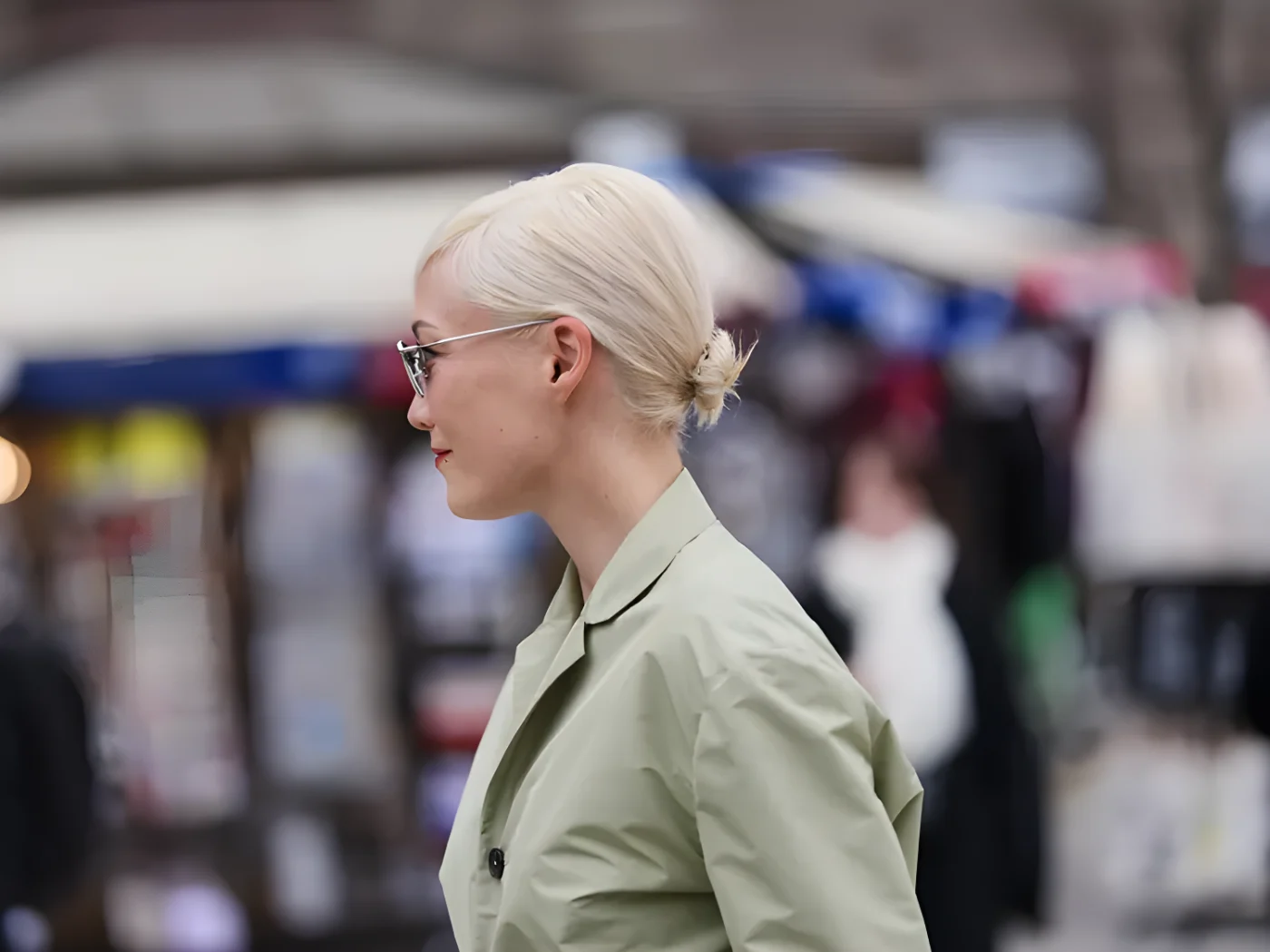 Pom Klementieff wears blonde hair with a short bang, black sunglasses, a light green cotton button front blazer, outside Jil Sander, during Milan Fashion Week