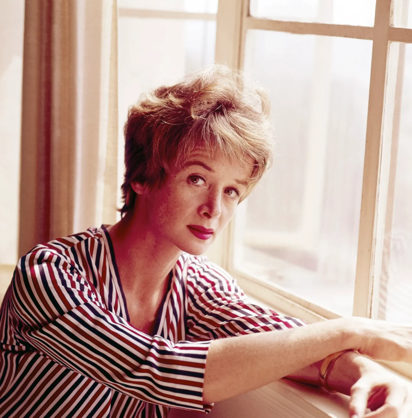 Portrait of Barbara Barrie sitting at a window, wearing a striped shirt.