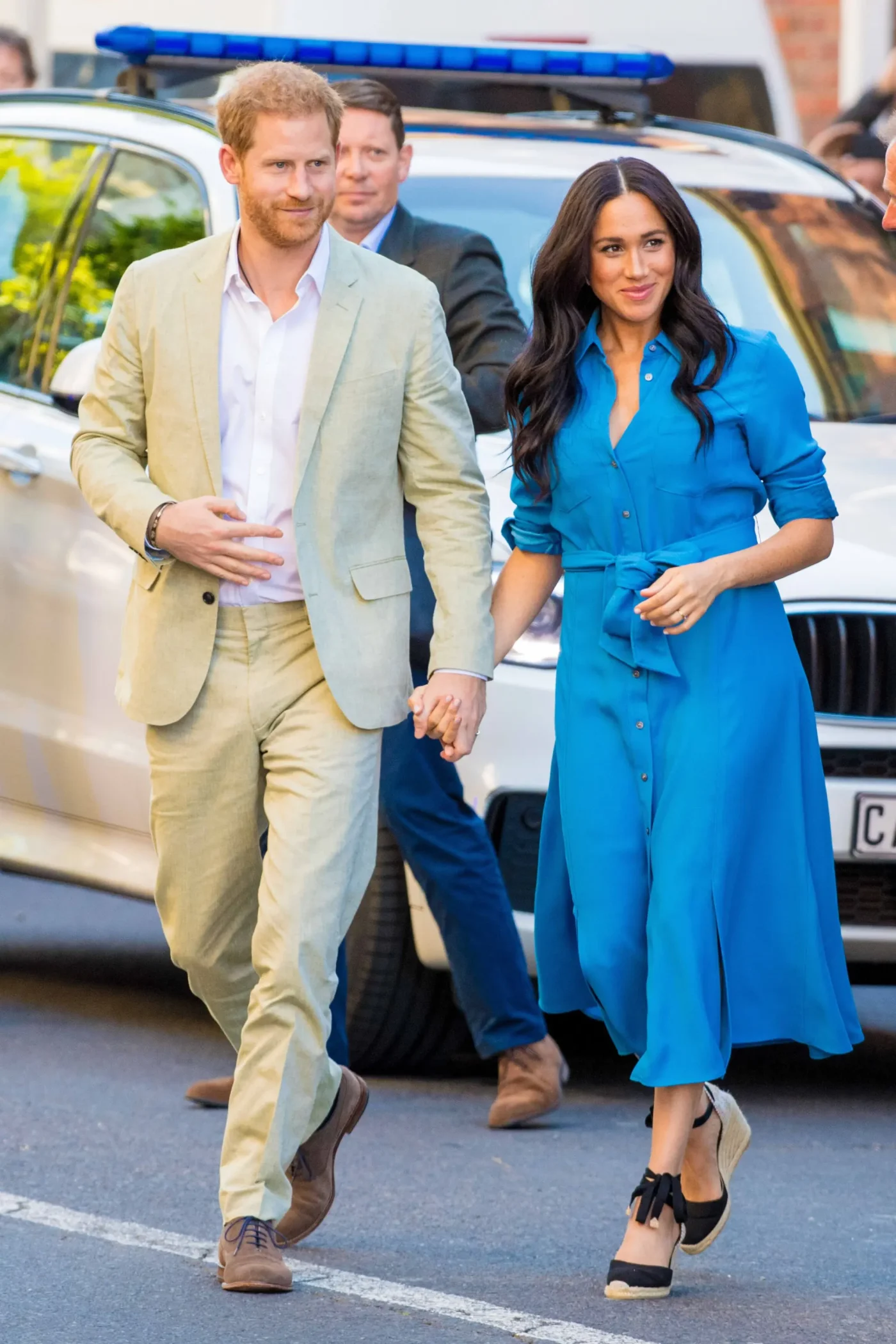 Prince Harry and Meghan Markle holding hands while walking outdoors.