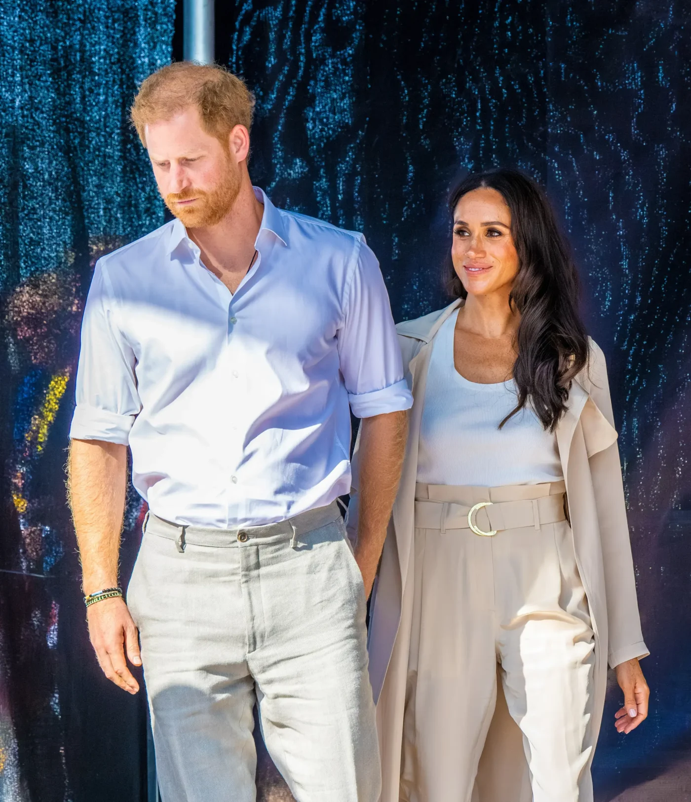 Prince Harry and Meghan Markle standing outdoors, with Prince Harry looking down and Meghan Markle smiling.