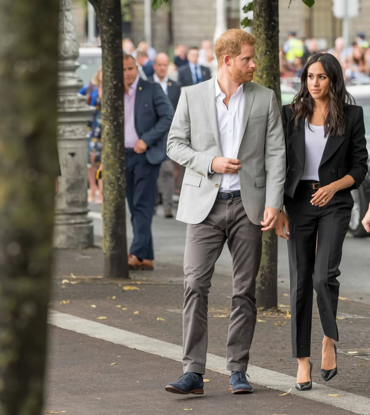 Prince Harry and Meghan Markle walking outside with security personnel in the background.