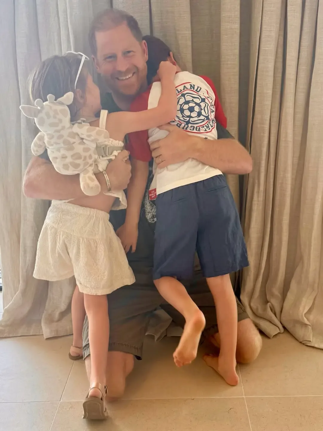 Prince Harry smiling while hugging his children, Prince Archie and Princess Lilibet.