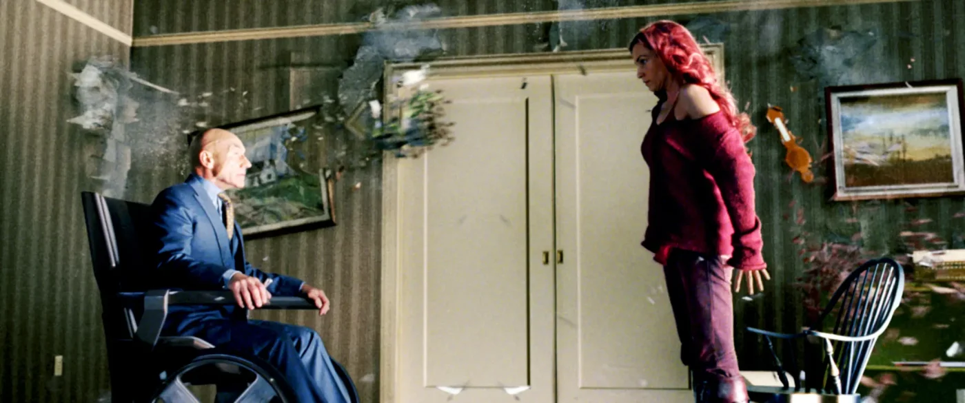 Professor X in his wheelchair and Jean Grey stand facing each other as objects disintegrate around them in a room.