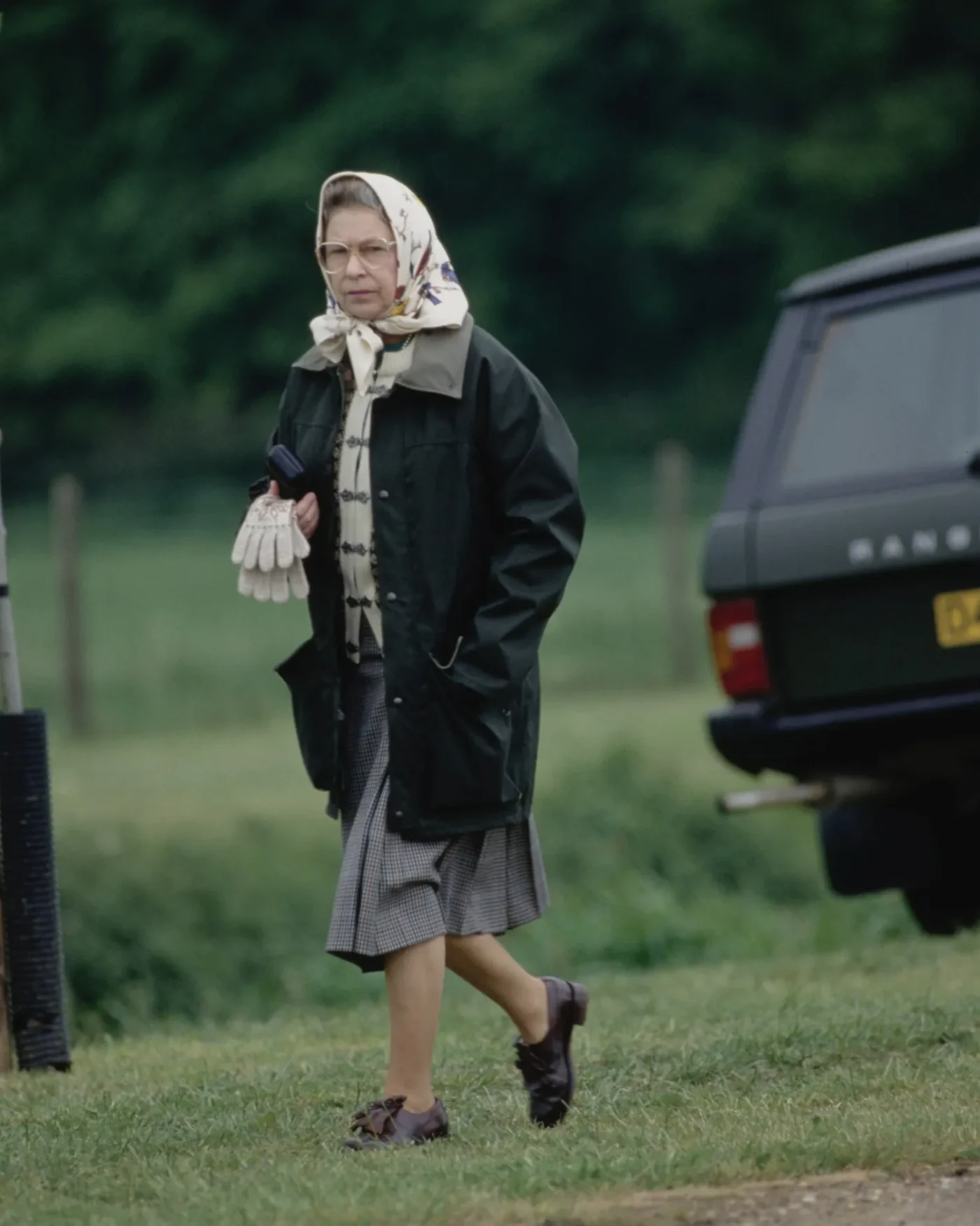 Queen Elizabeth II, wearing a green waxed jacket, grey skirt and a headscarf, attends the Royal Windsor Horse Show, held at Home Park on the Royal estate at Windsor, Berkshire, England, 12th May 1990.