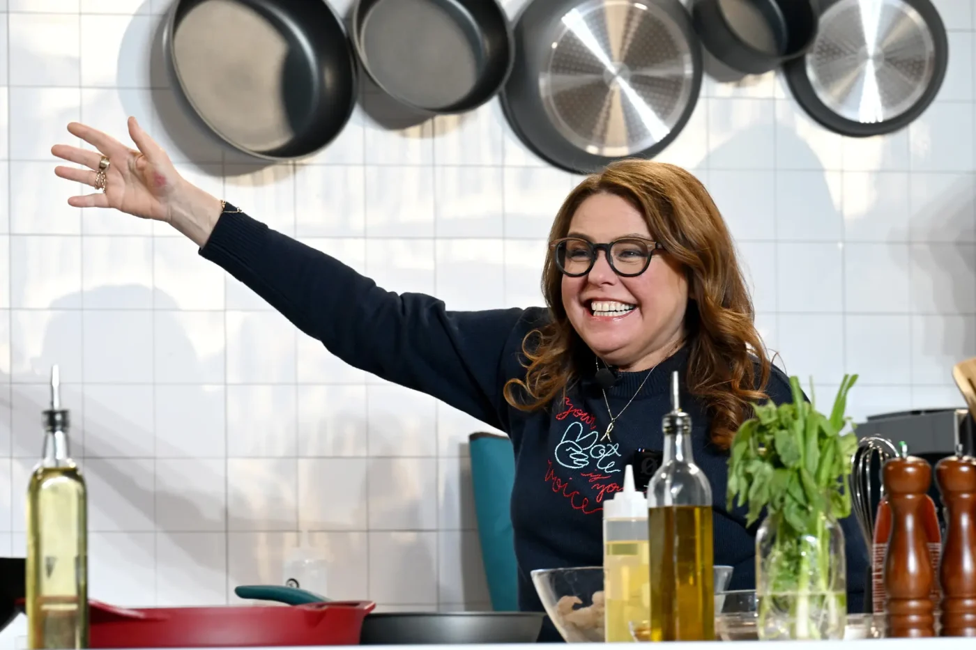 Rachael Ray smiling and waving onstage during a culinary demonstration.