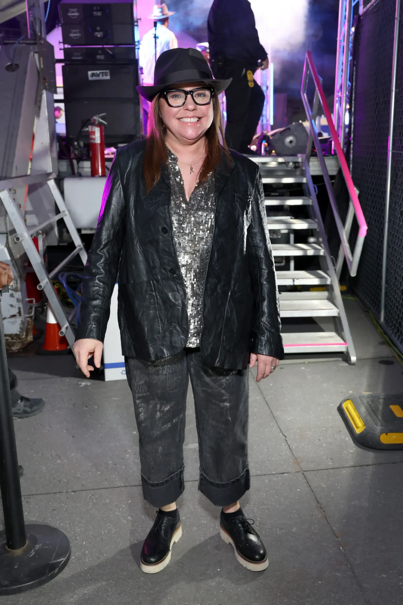 Rachael Ray wearing a black hat, black jacket, and glasses at an event.